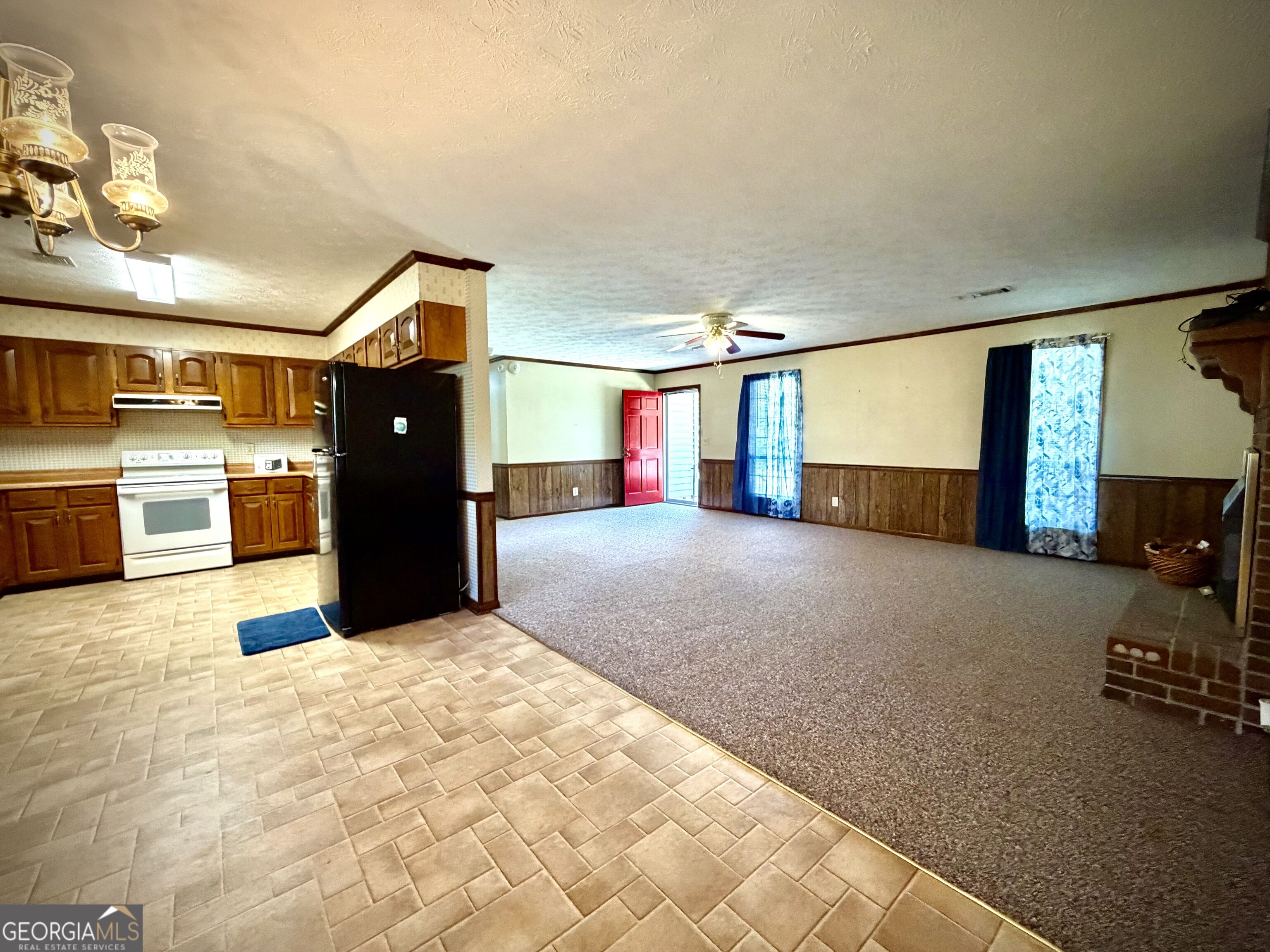 Open kitchen and living room with wood cabinets, tiled floor, carpet, and brick fireplace.