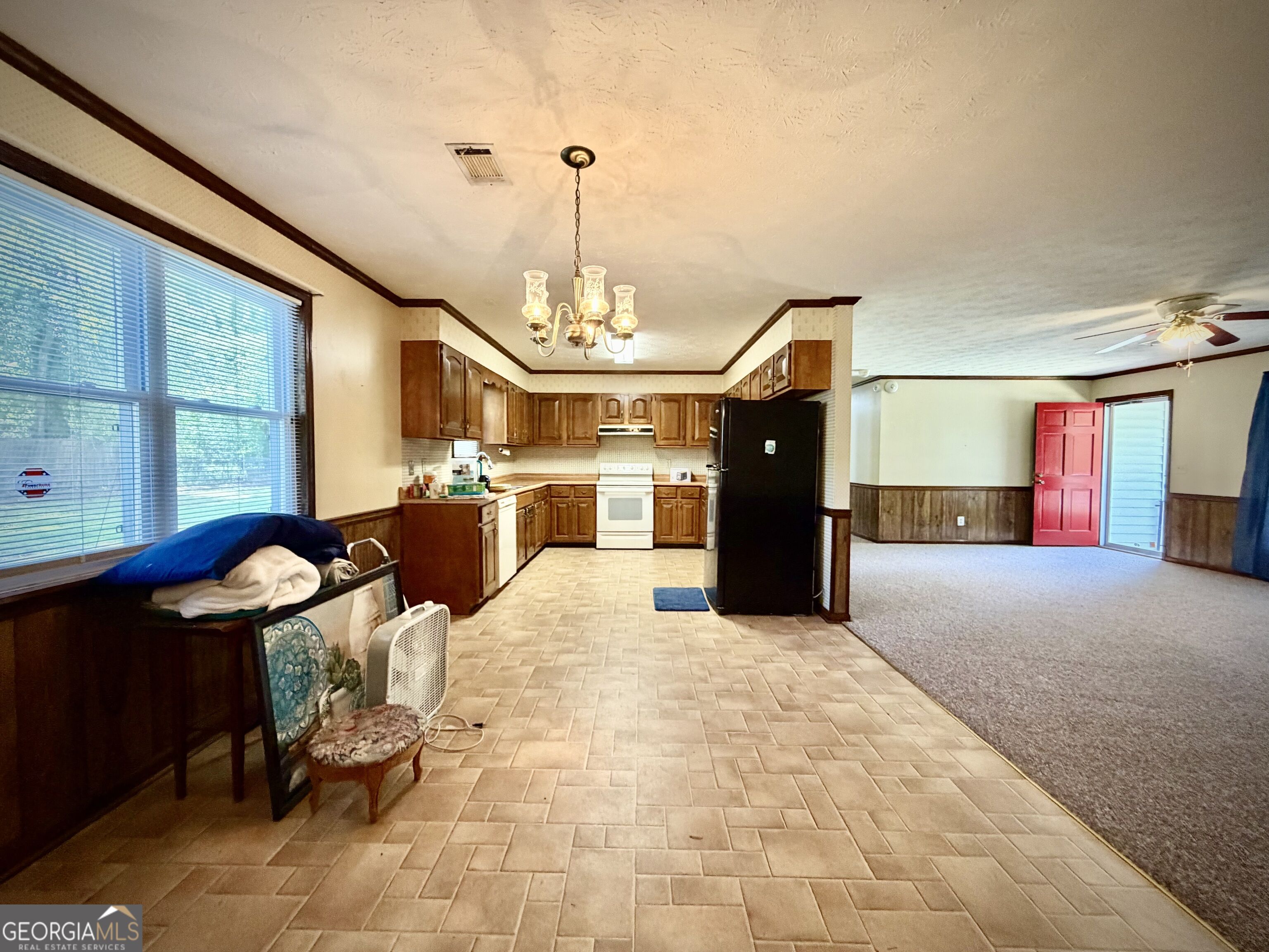 Kitchen with dark wood cabinets and tiled floor opening into a carpeted living area with a red door.