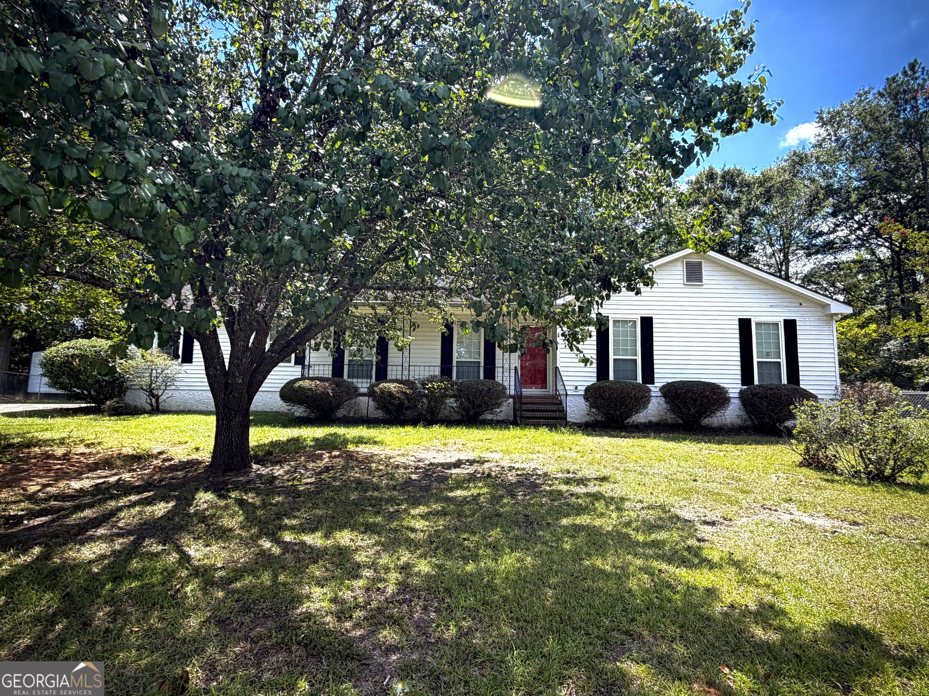 White single-story house with a red front door, shaded by a large tree.
