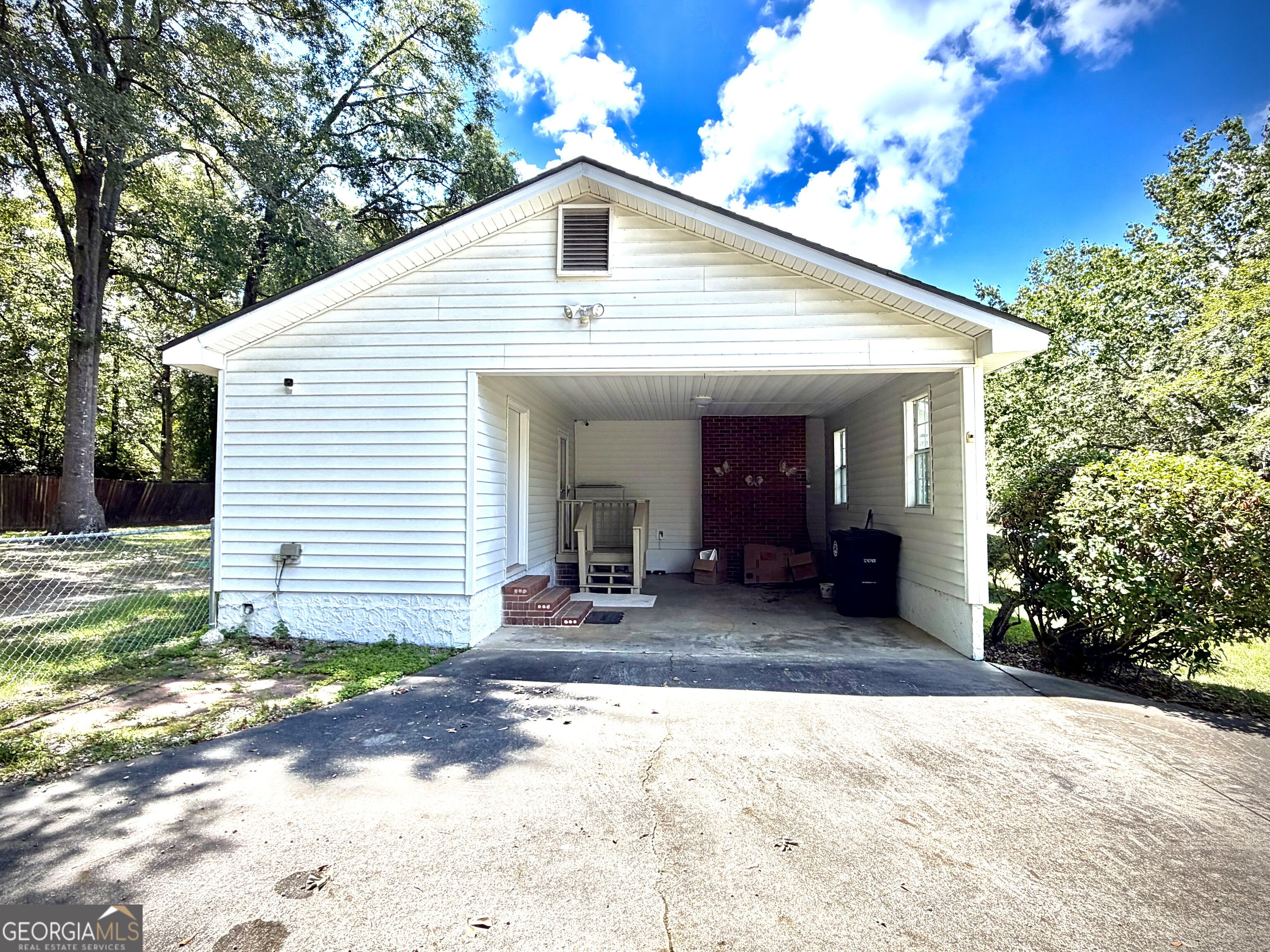 White-sided home with an open carport, brick accent wall, and broad concrete driveway.