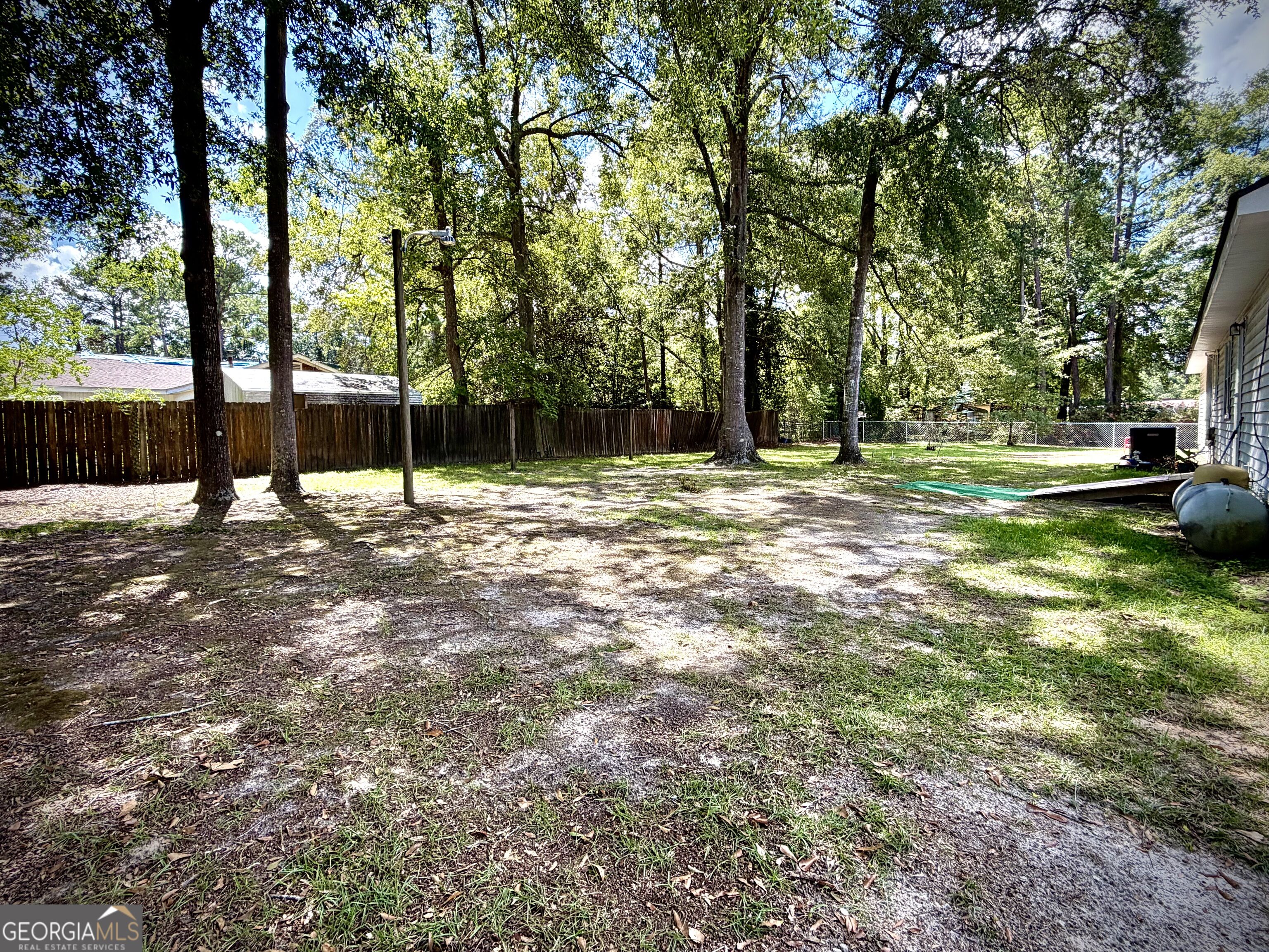 Shaded backyard with mature trees, patchy grass, and wood and chain-link fencing.