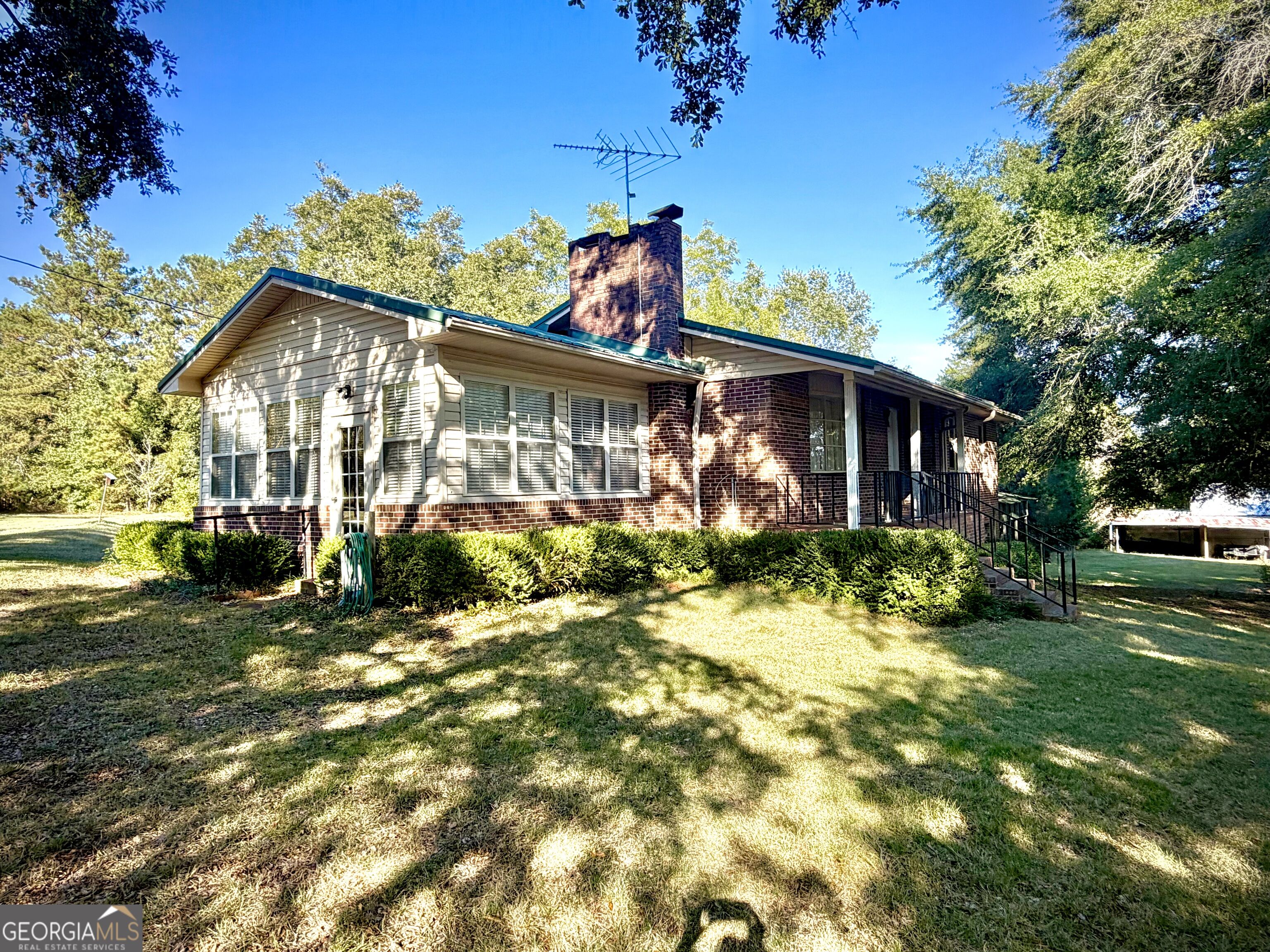 Single-story brick and sided home with a tall chimney, raised porch, and mature trees.