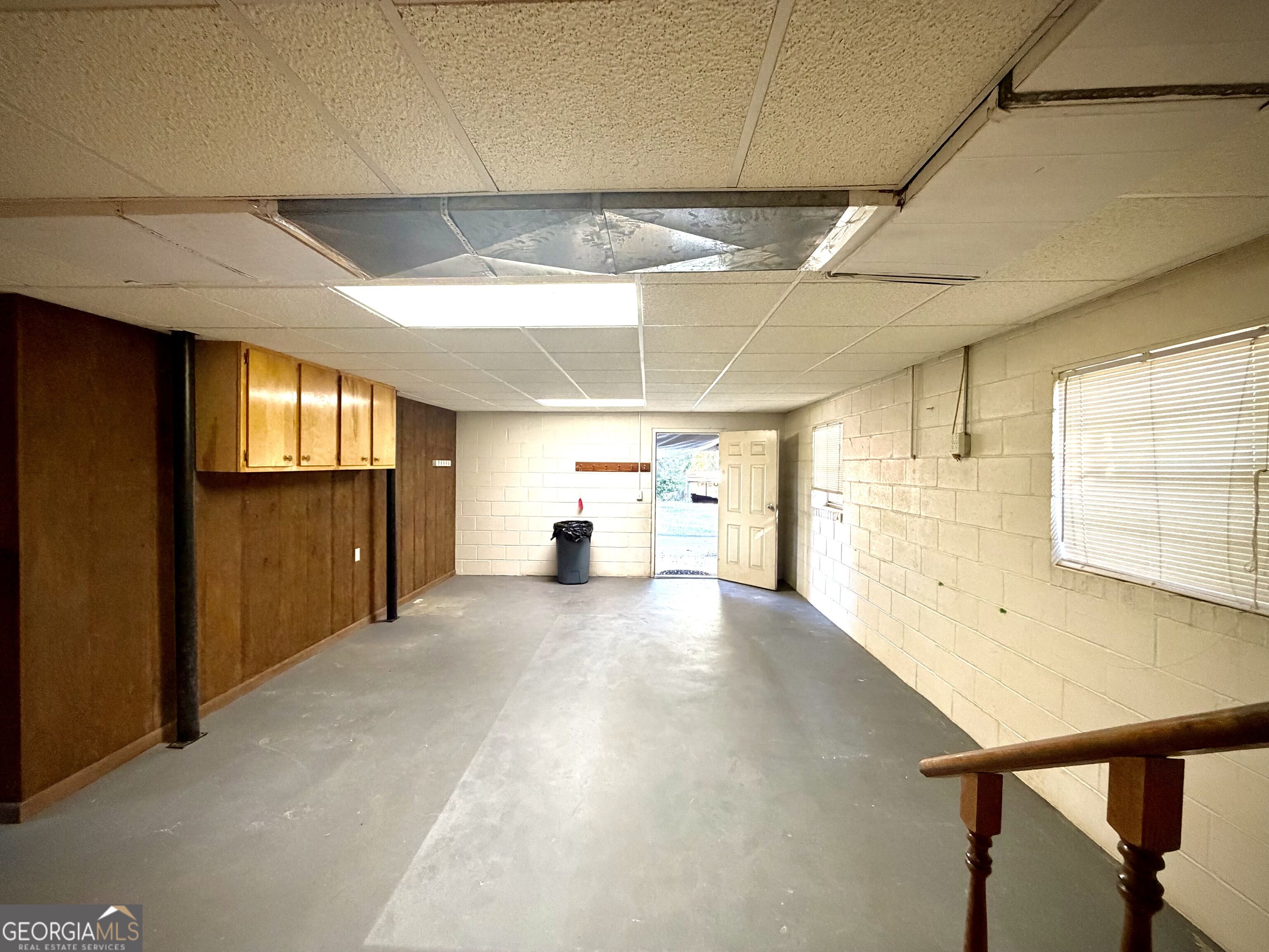 Empty garage with overhead cabinets, block walls, and a damaged drop ceiling.