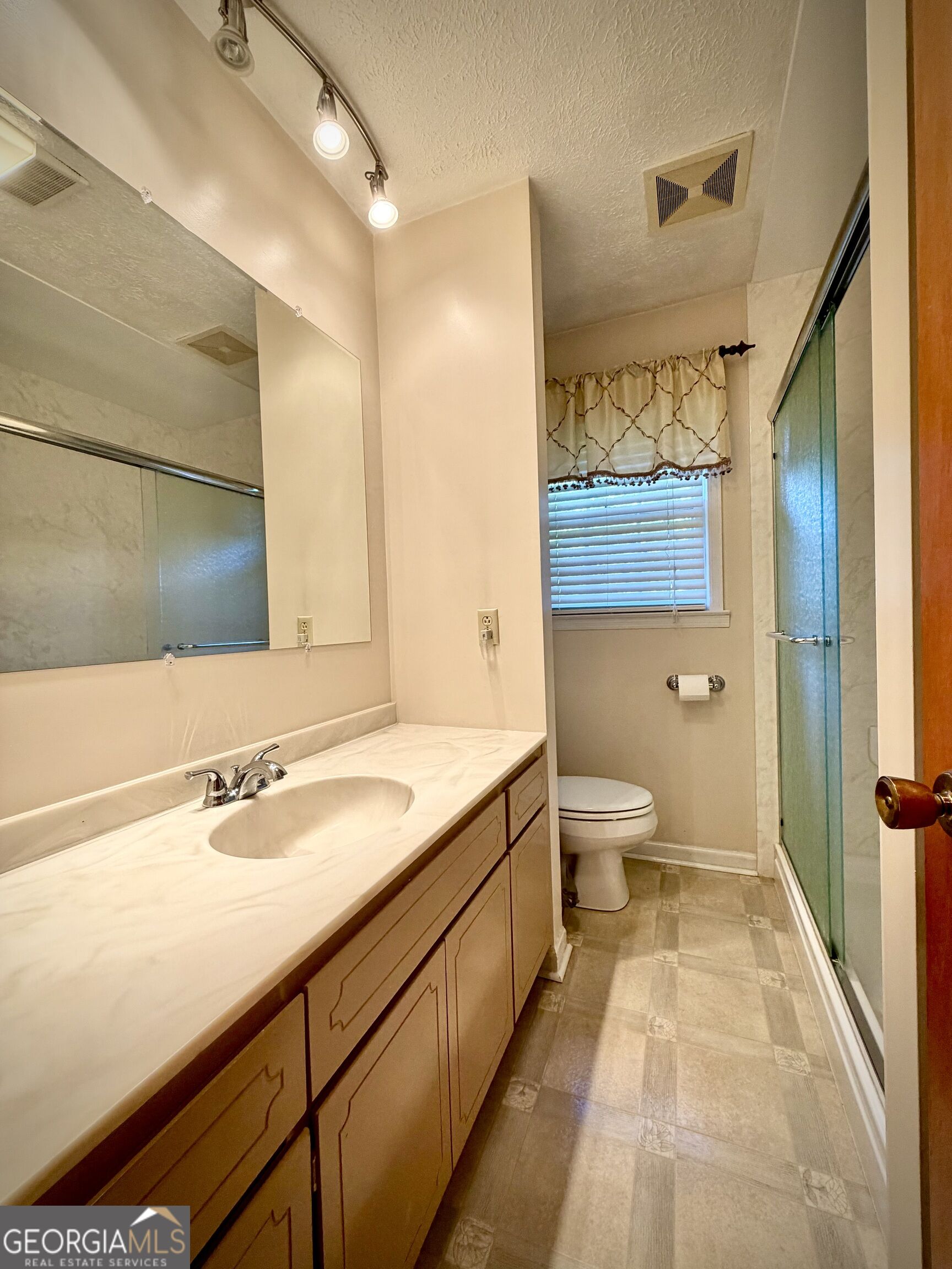Bathroom with a long wood vanity, large mirror, toilet, and glass-enclosed shower.