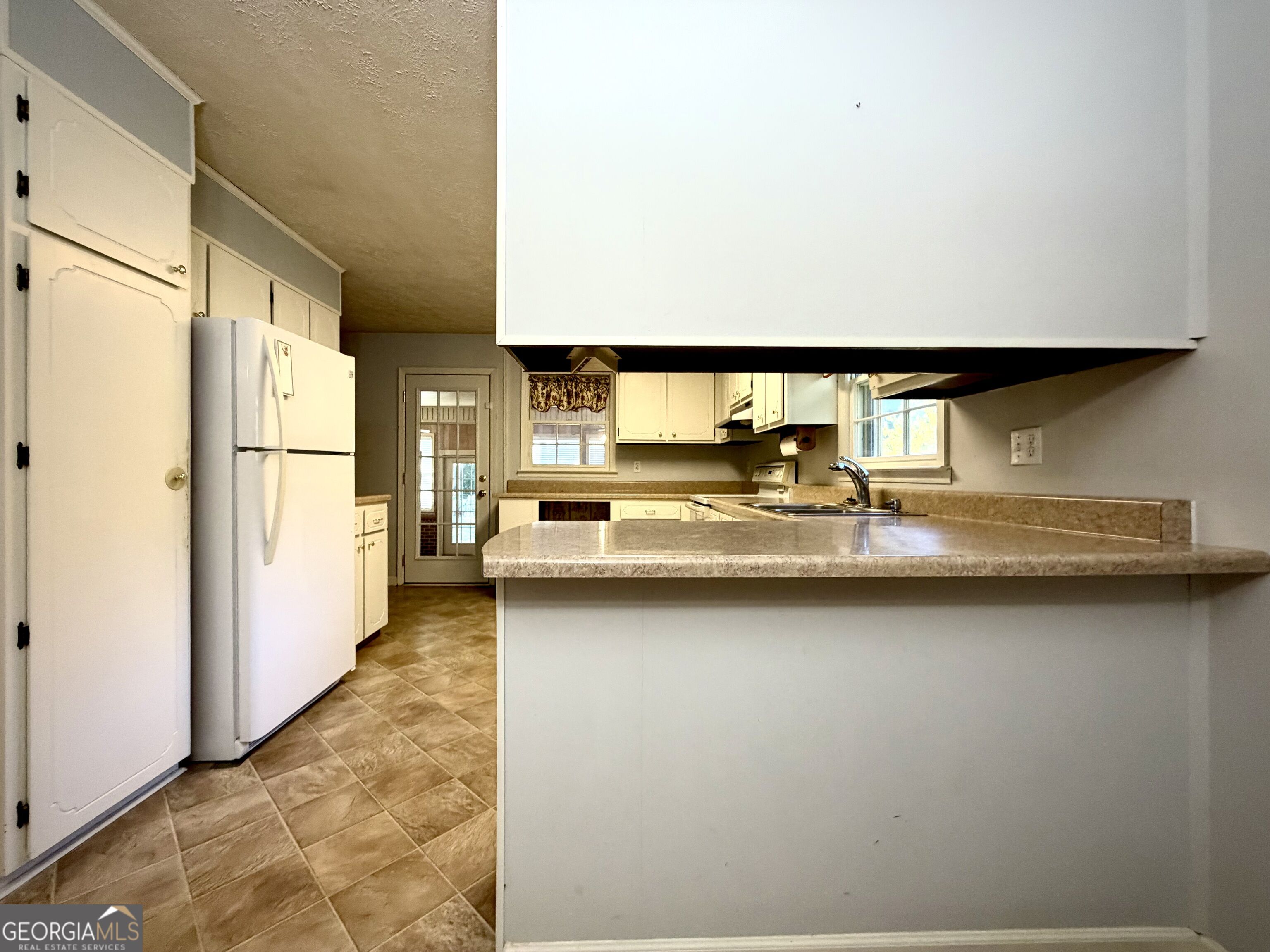 Kitchen with white cabinets, a long countertop peninsula, and tan tile flooring.