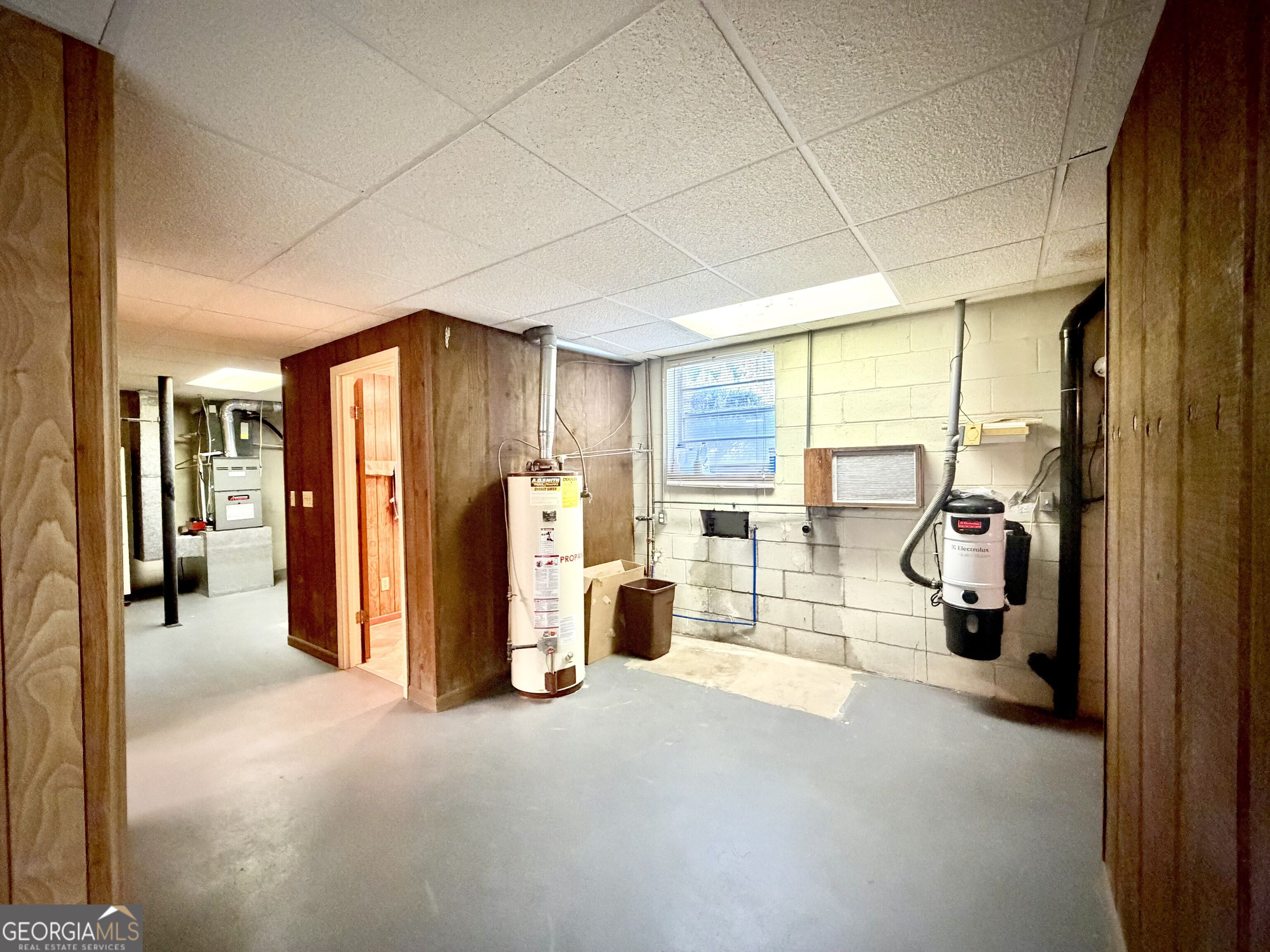 Basement utility room with a water heater, furnace, exposed pipes, and a wooden sauna enclosure.