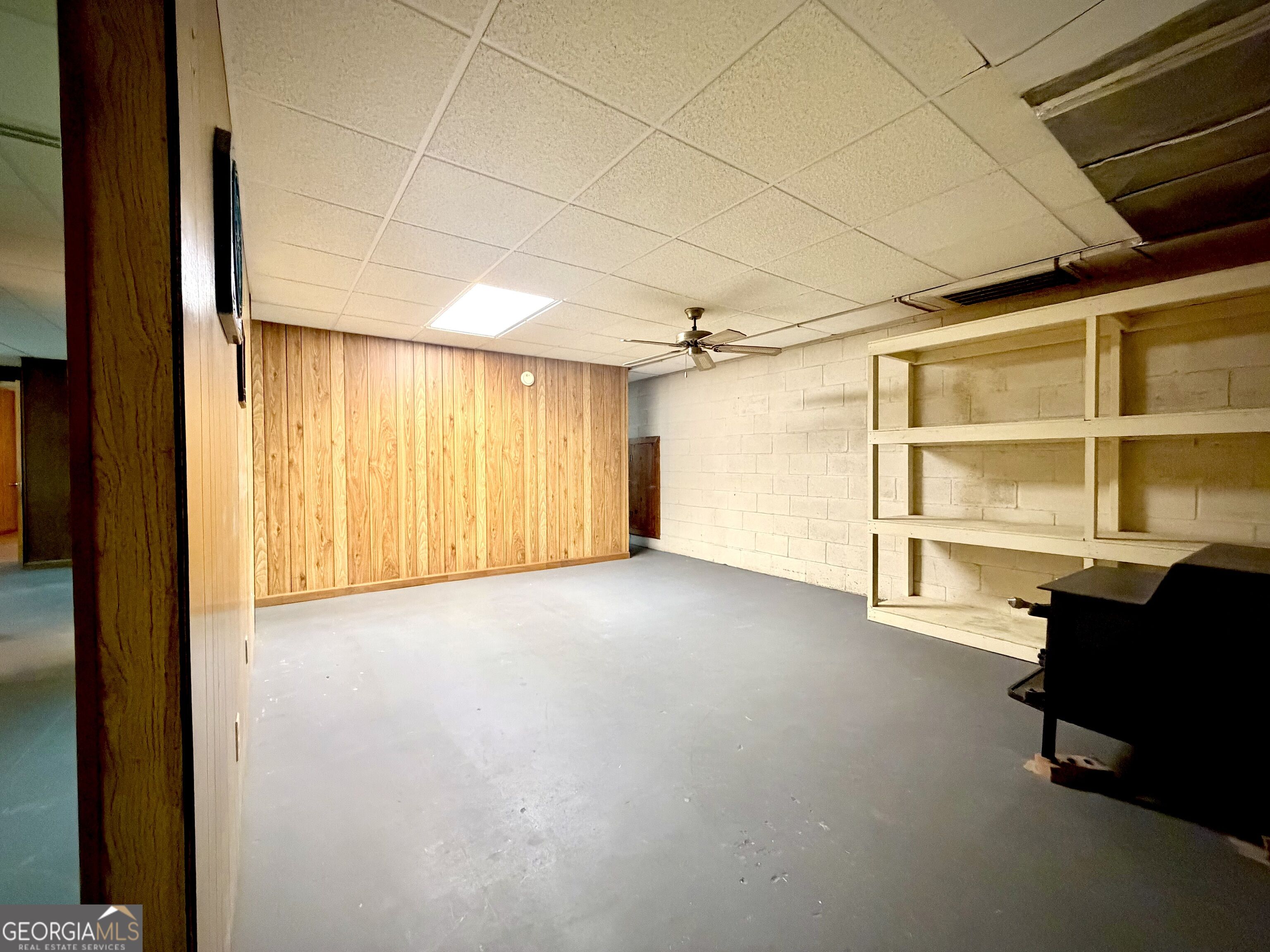 Basement room with wood paneling, built-in open shelving, and a gray concrete floor.