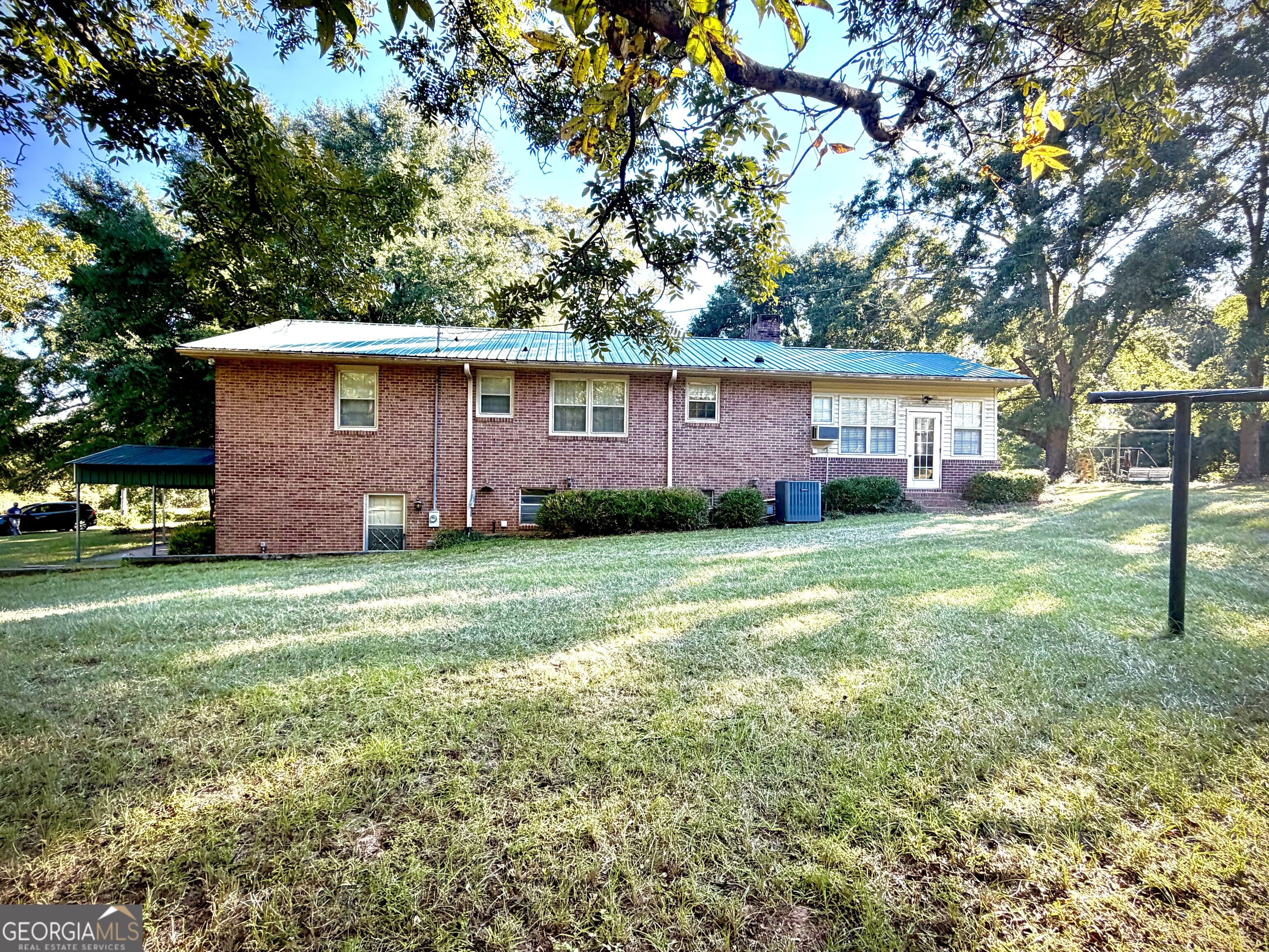 Brick ranch home with a metal roof, shaded lawn, and covered carport.