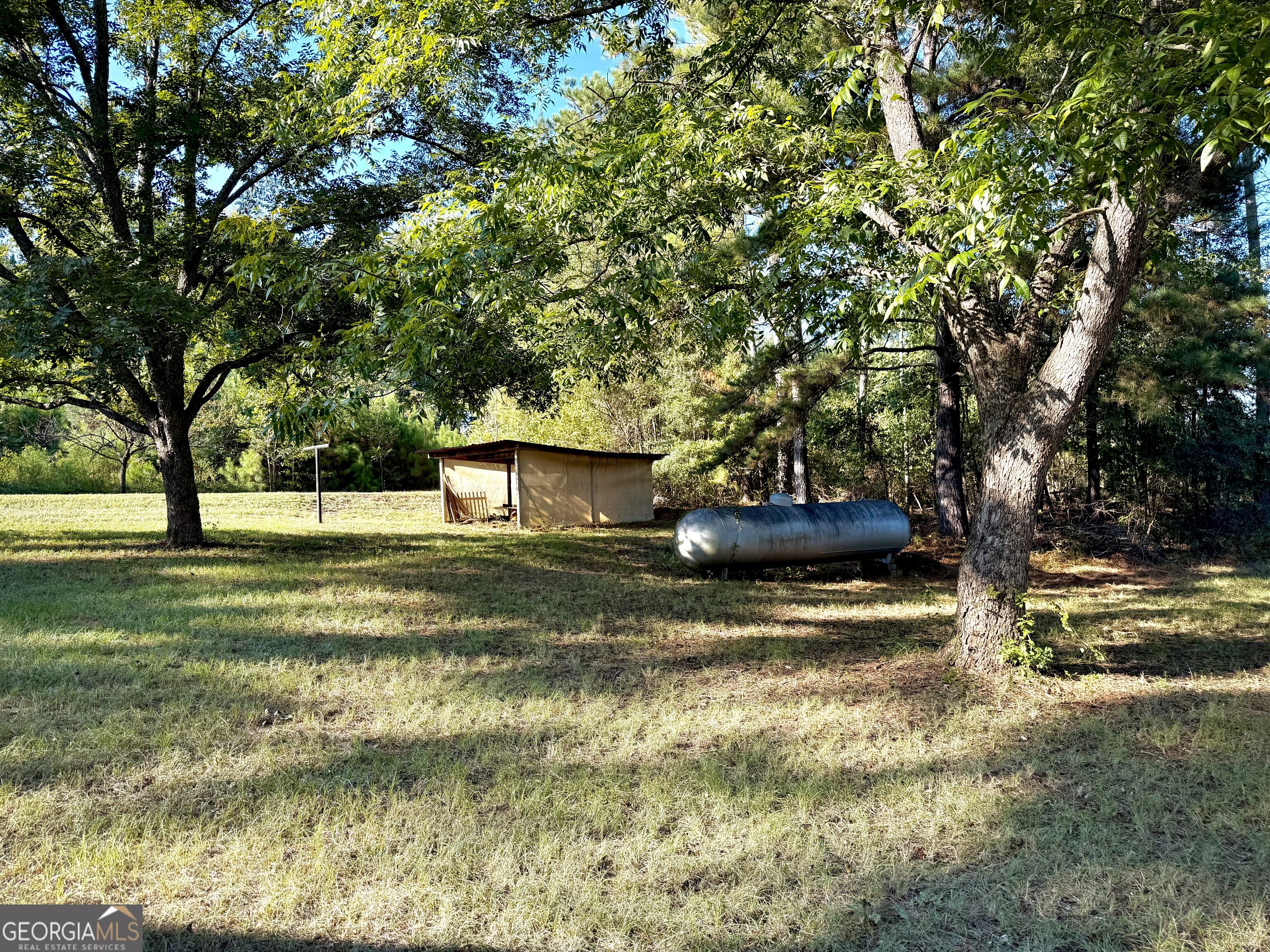 Tree-shaded grassy yard with a small shed and horizontal propane tank.