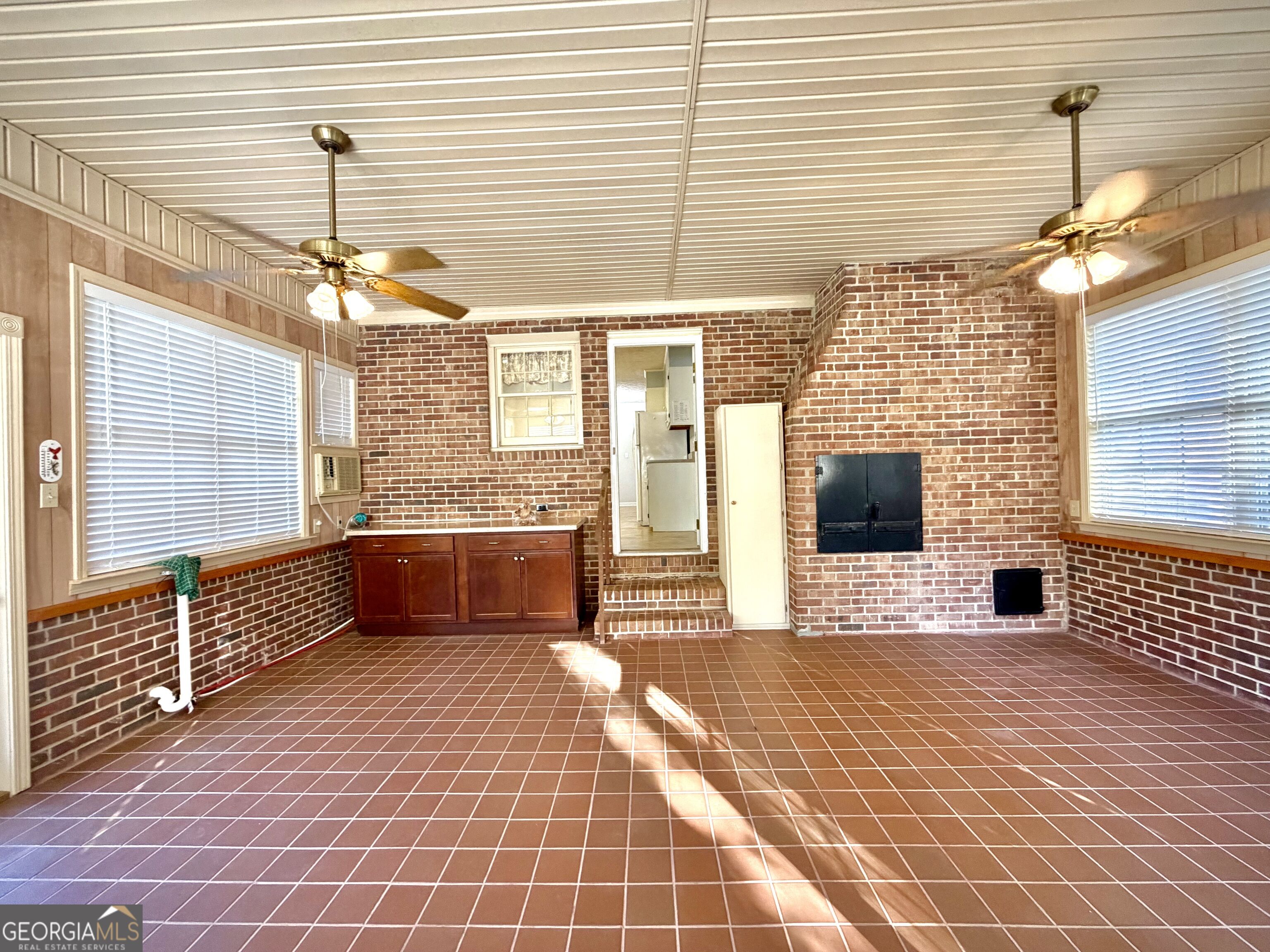 Sunroom with brick walls, tiled floor, large windows, and a brick fireplace.