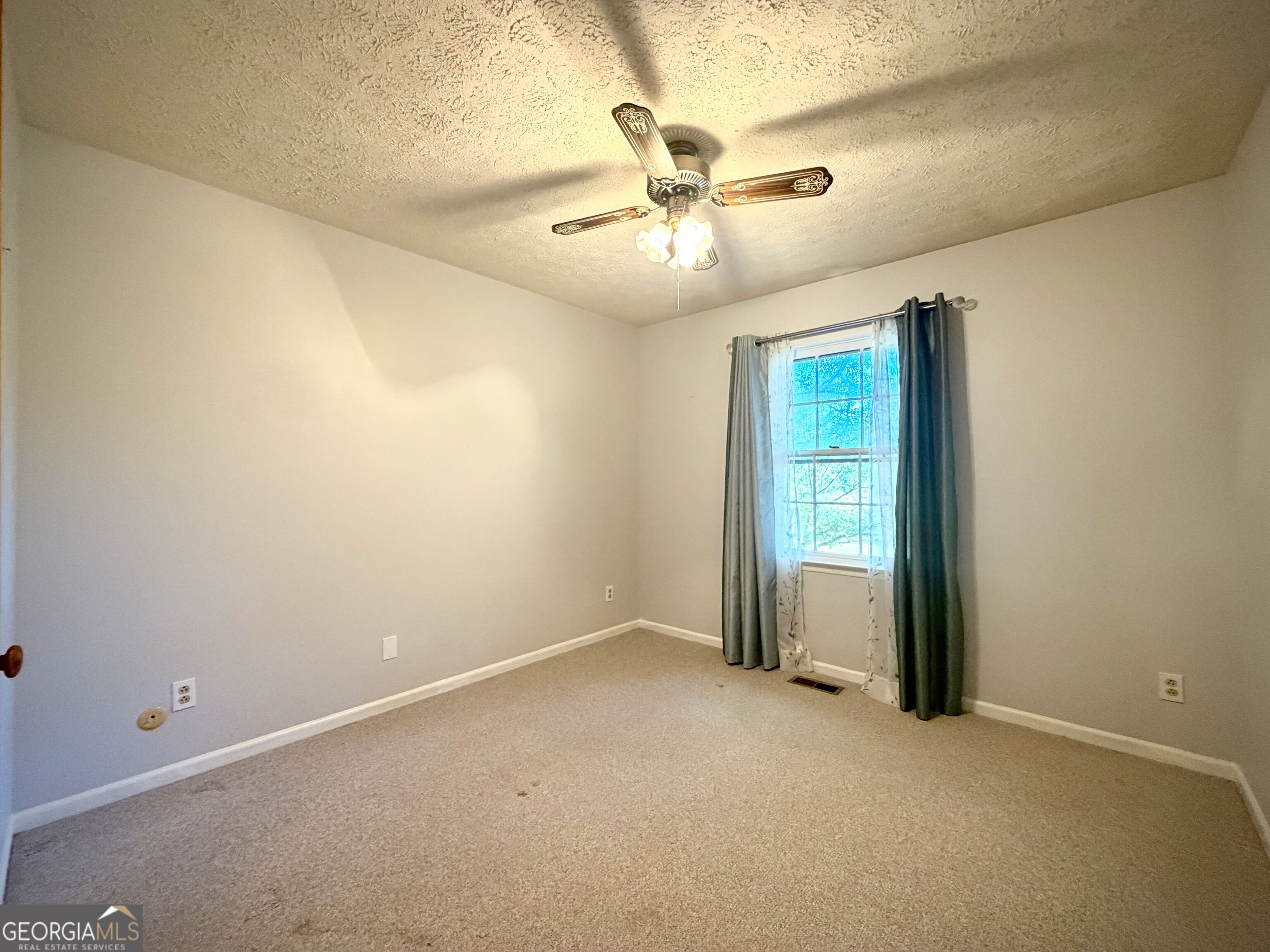 Empty bedroom with beige carpet, ceiling fan, and curtained window.