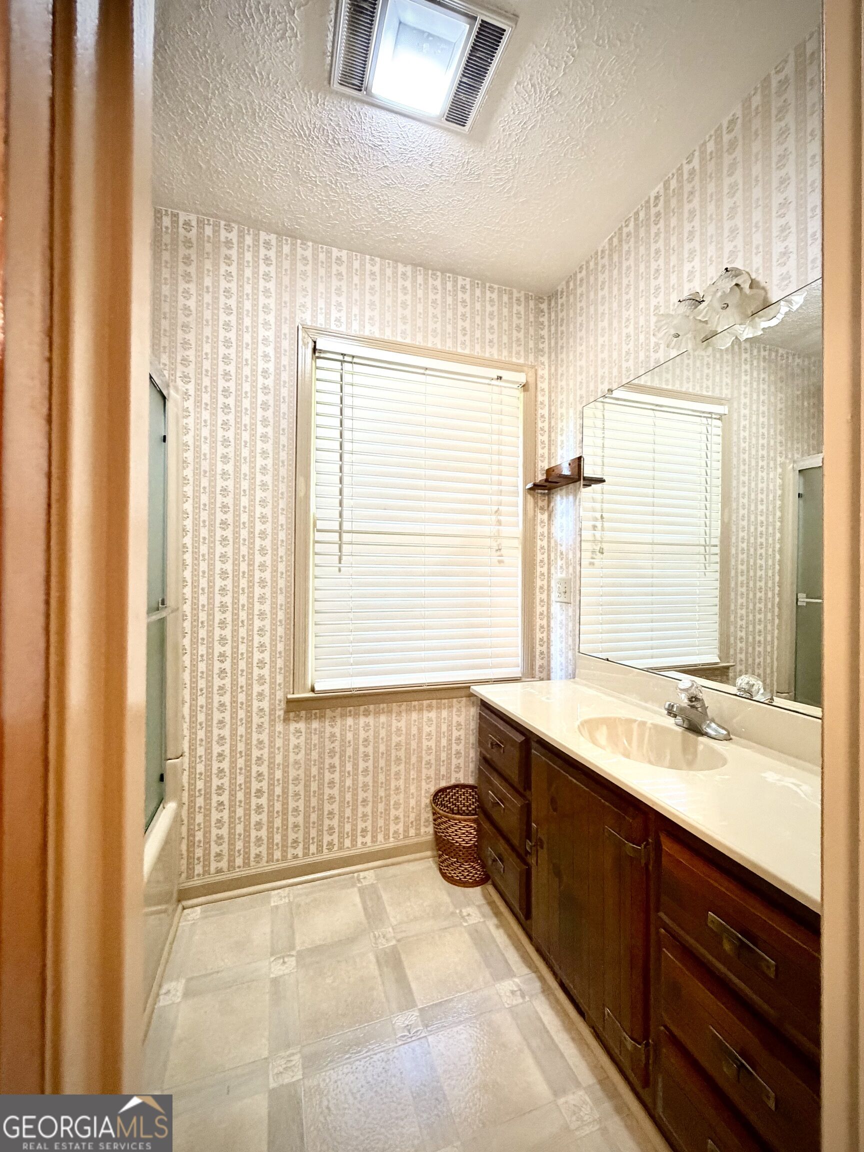 Bathroom with patterned wallpaper, a large mirror, and a dark wood vanity with a single sink.