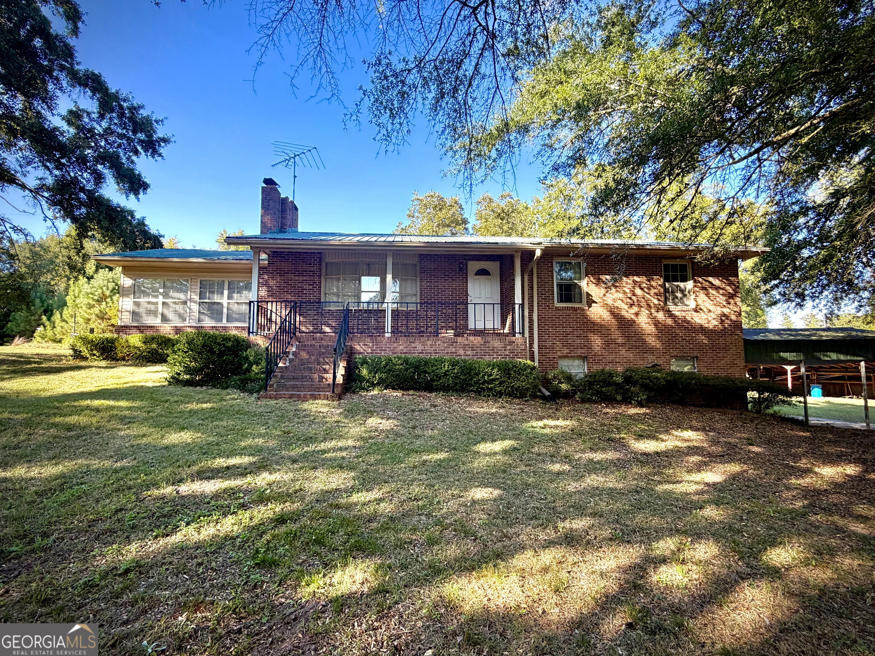 Brick house with a covered porch and front steps beneath mature shade trees.