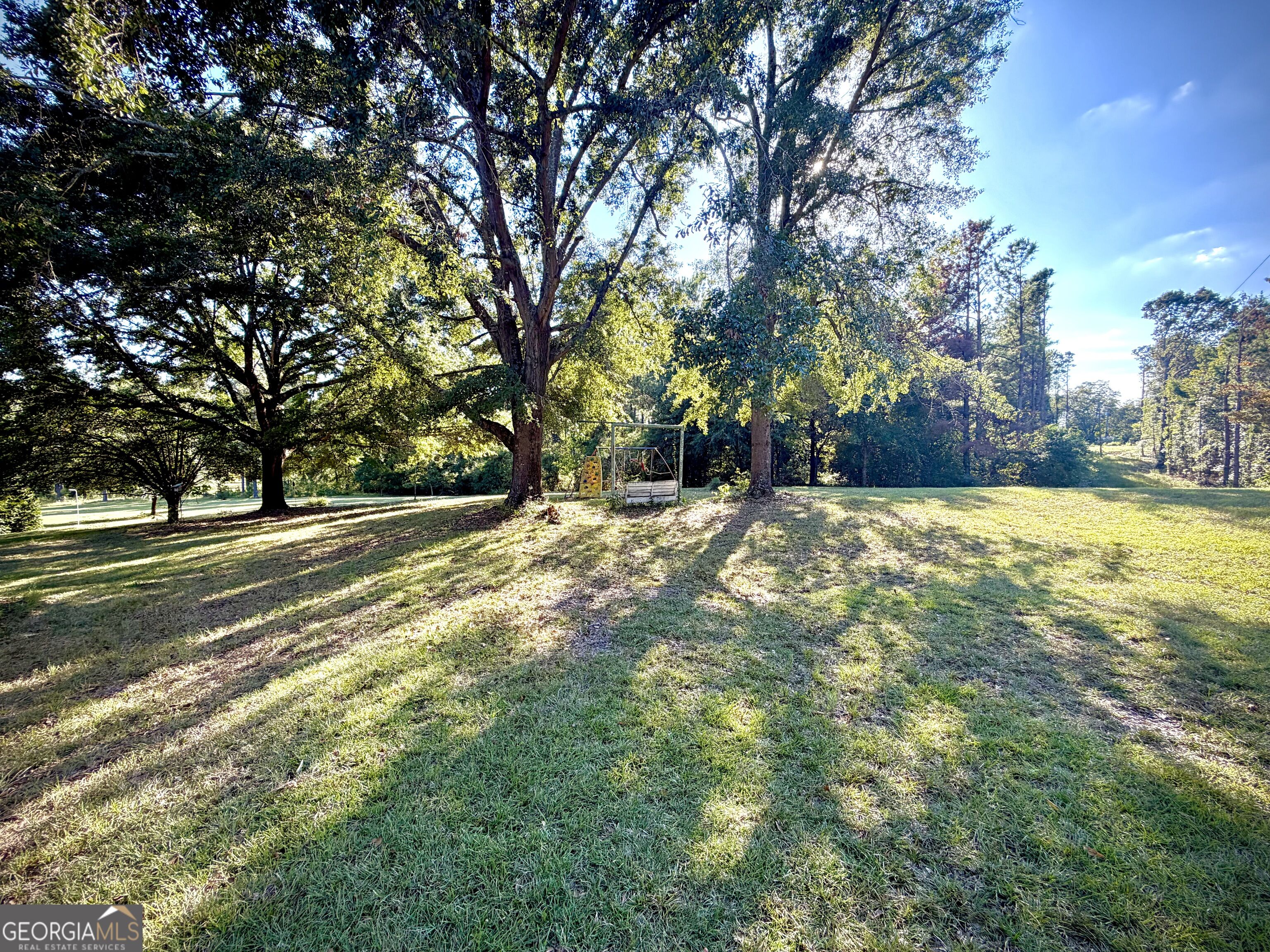 Spacious grassy yard with mature shade trees and a small playset.