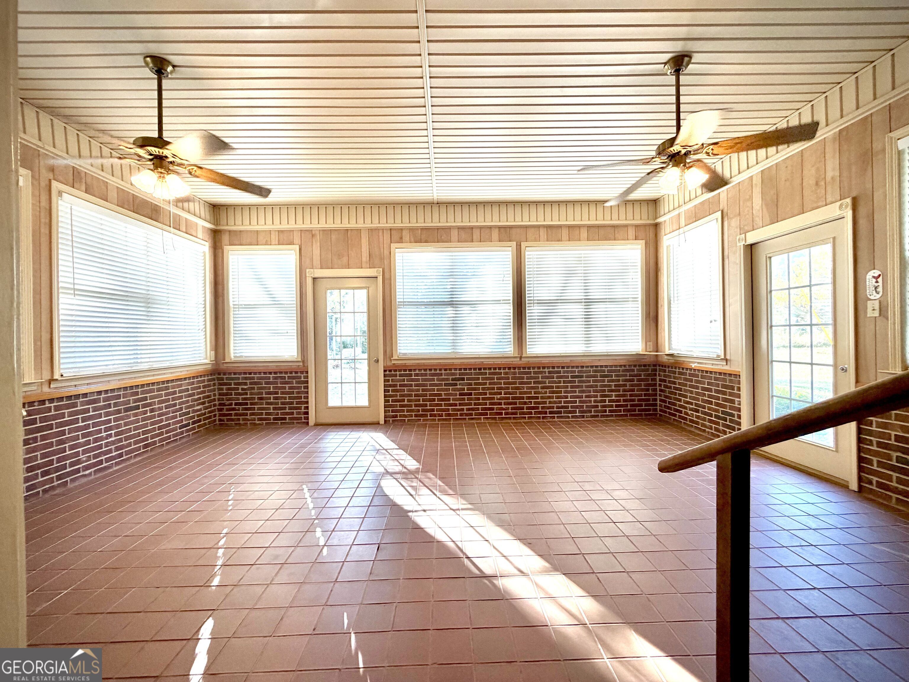 Bright enclosed sunroom with tiled floor, brick wainscoting, ceiling fans, and multiple windows.