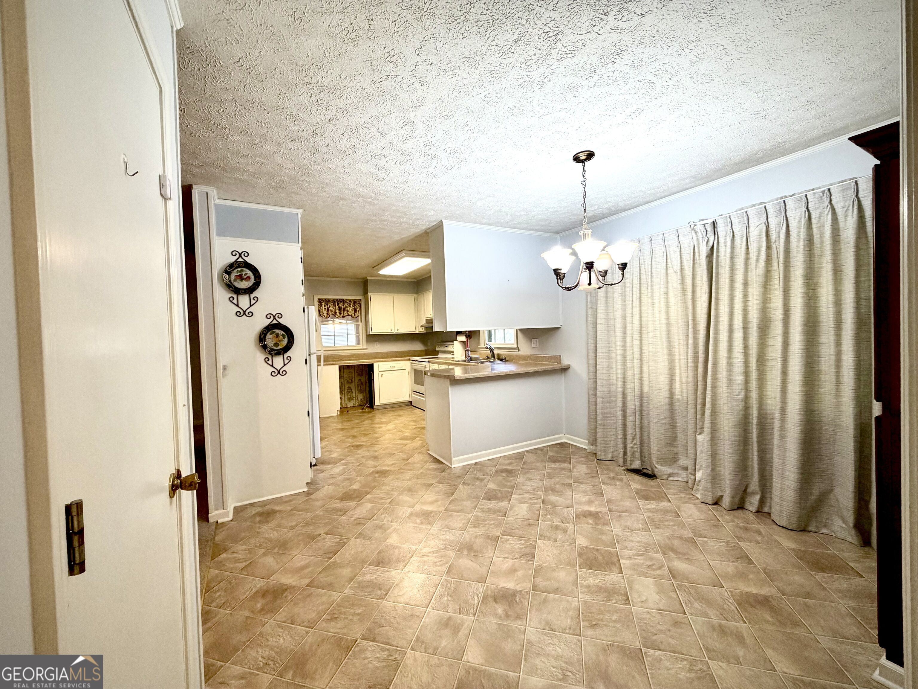 Dining area with tiled floor, chandelier, and open kitchen with peninsula.