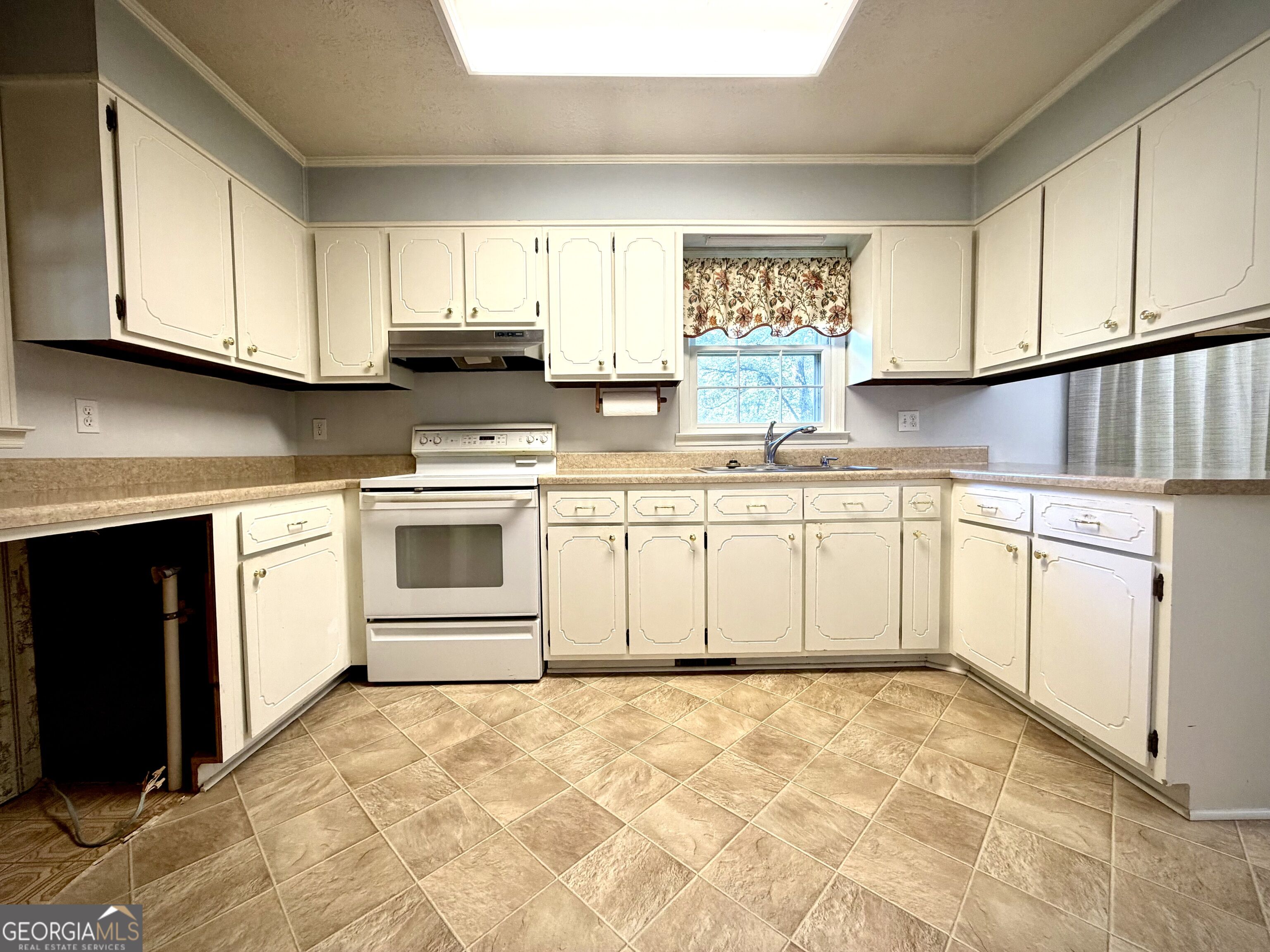 Kitchen with cream cabinets, tan tile flooring, and a window above the sink.
