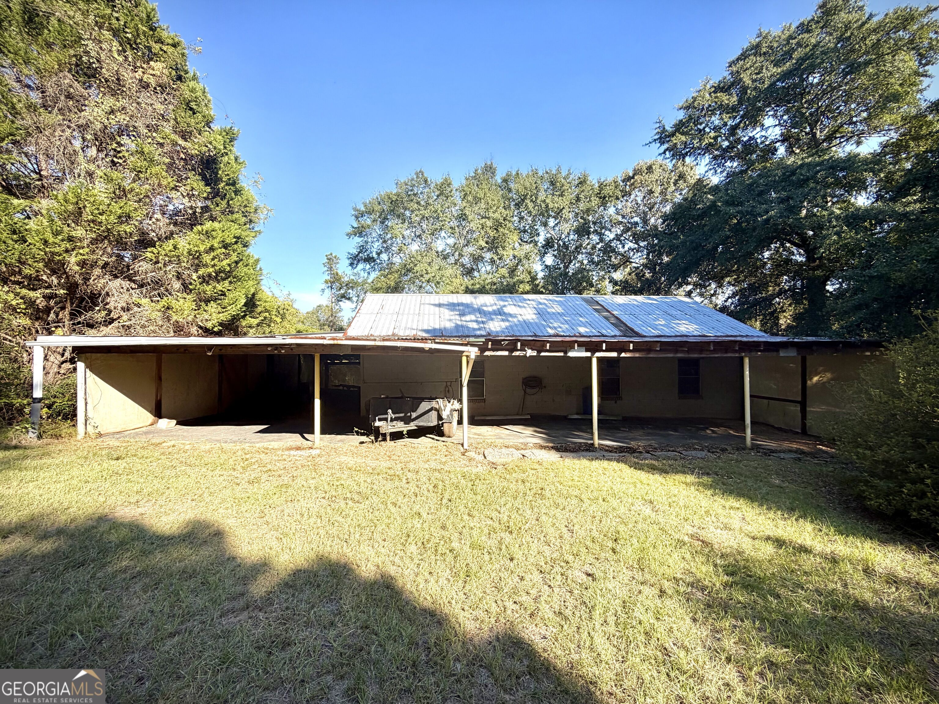 Single-story rural property with a broad metal roof, deep covered porch, and grassy yard.