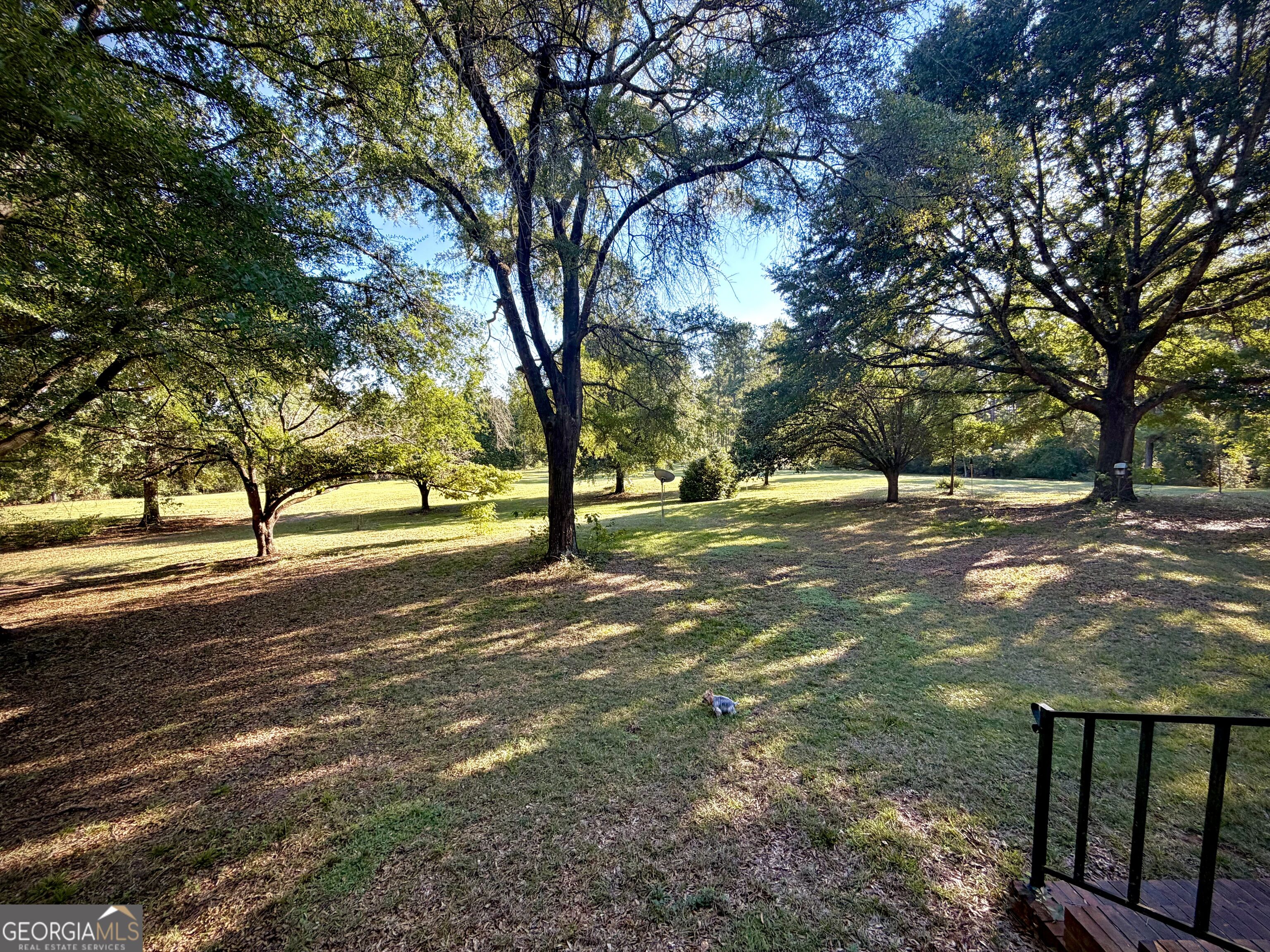 Spacious tree-shaded lawn with a small deck and black railing.