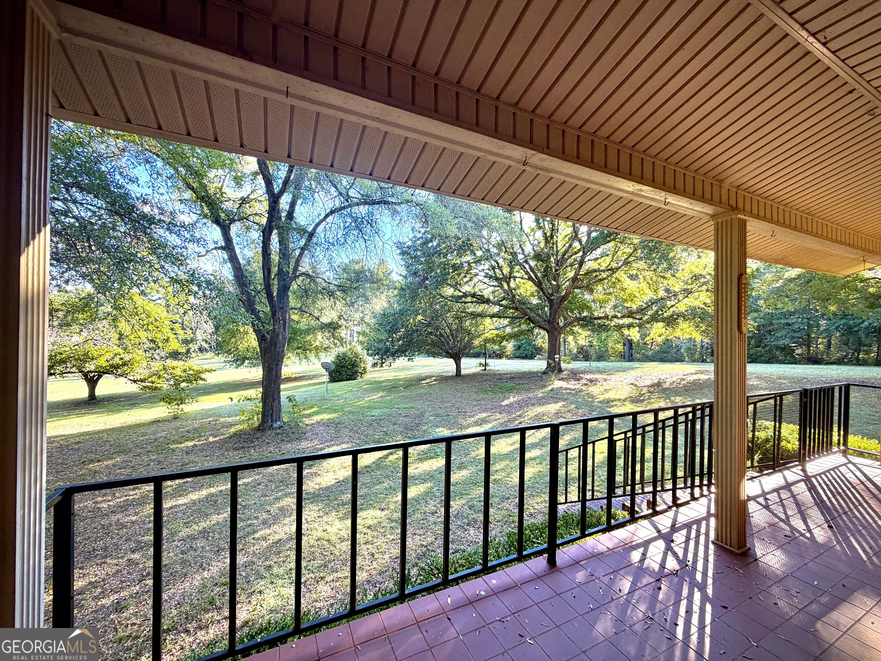 Covered porch overlooking a spacious lawn shaded by mature trees.