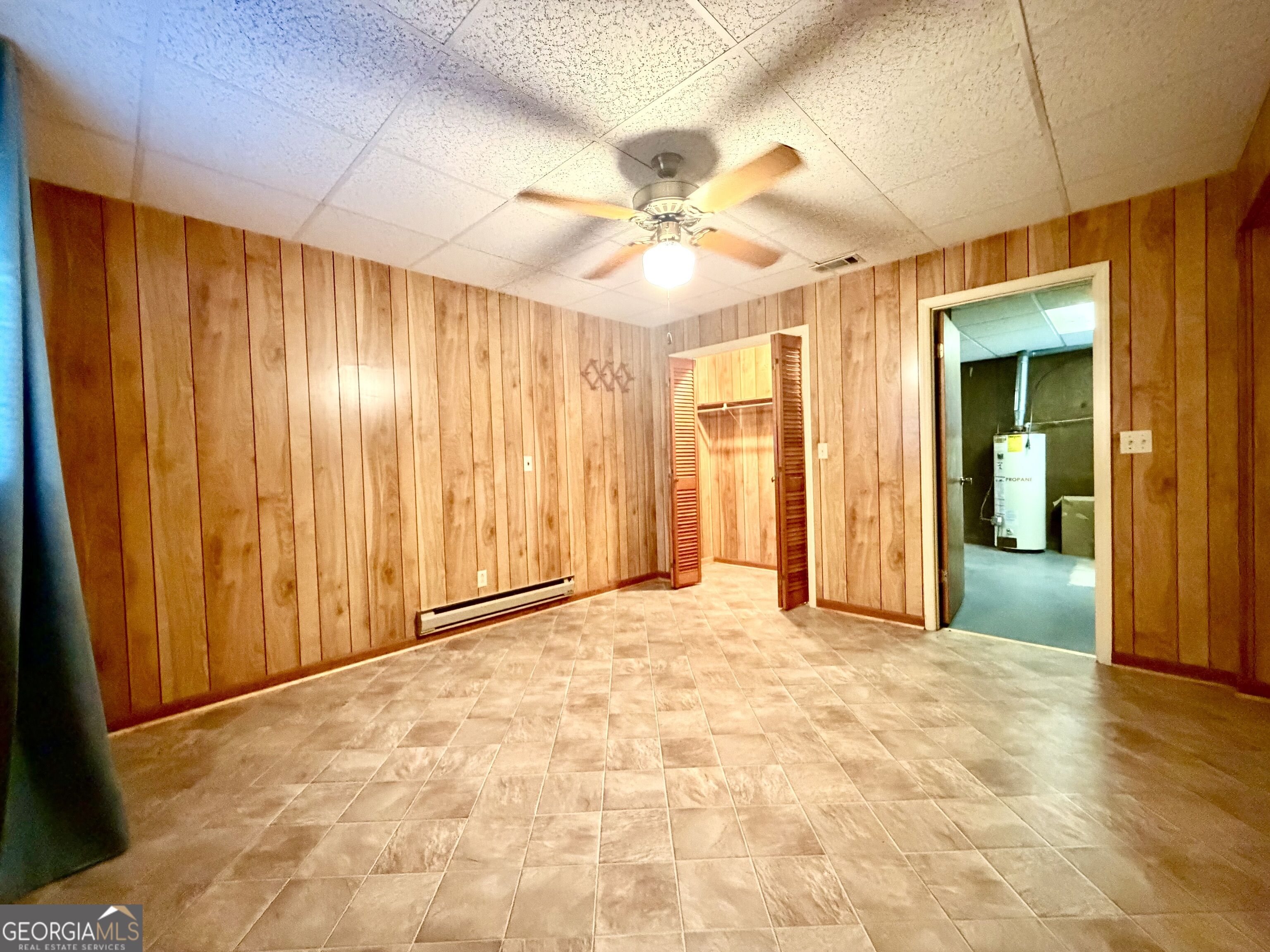 Empty wood-paneled room with tiled floor, open closet, and doorway to a utility room.