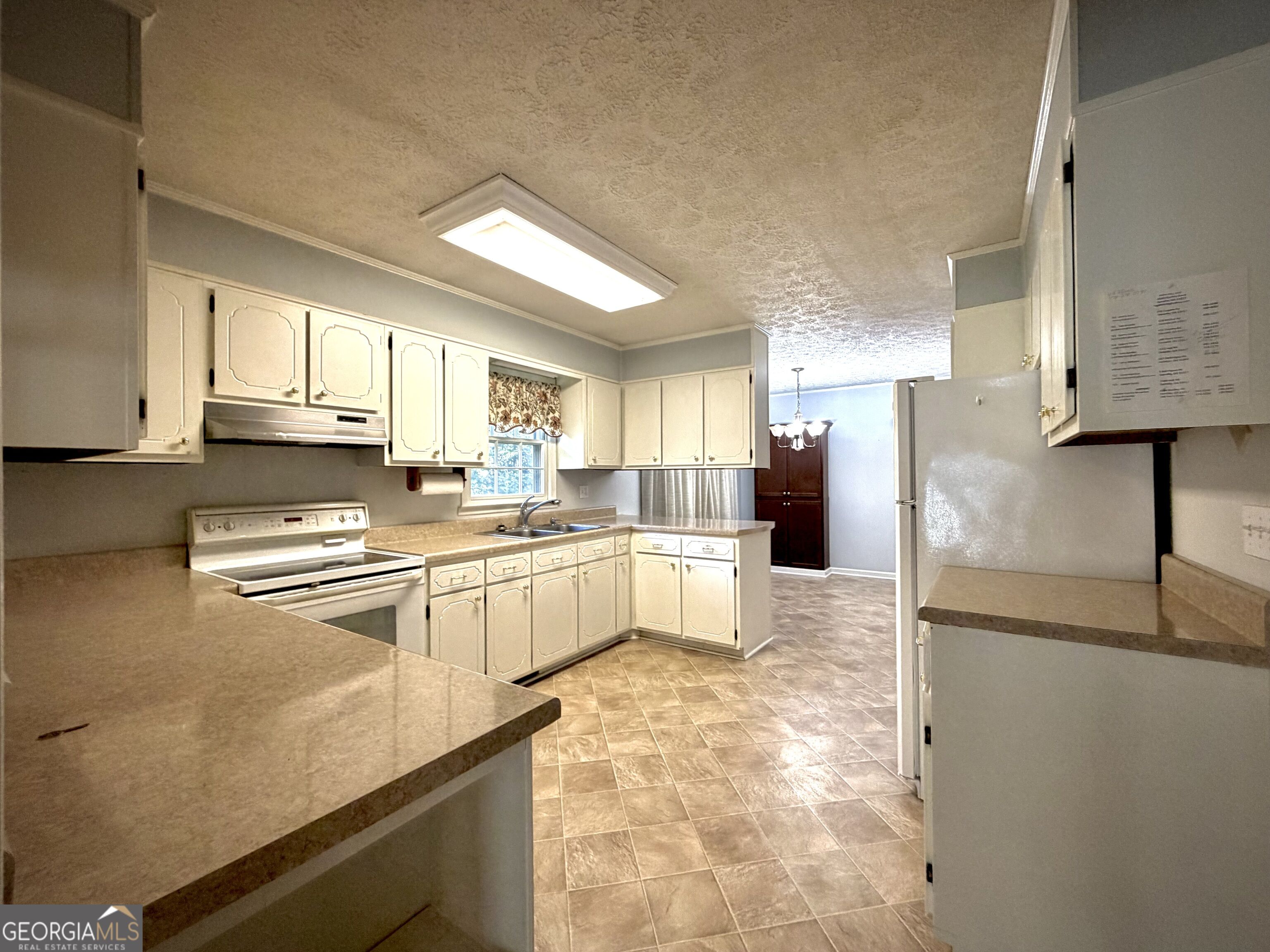 Kitchen with cream cabinets, tan counters, tiled floor, and an adjoining dining area.
