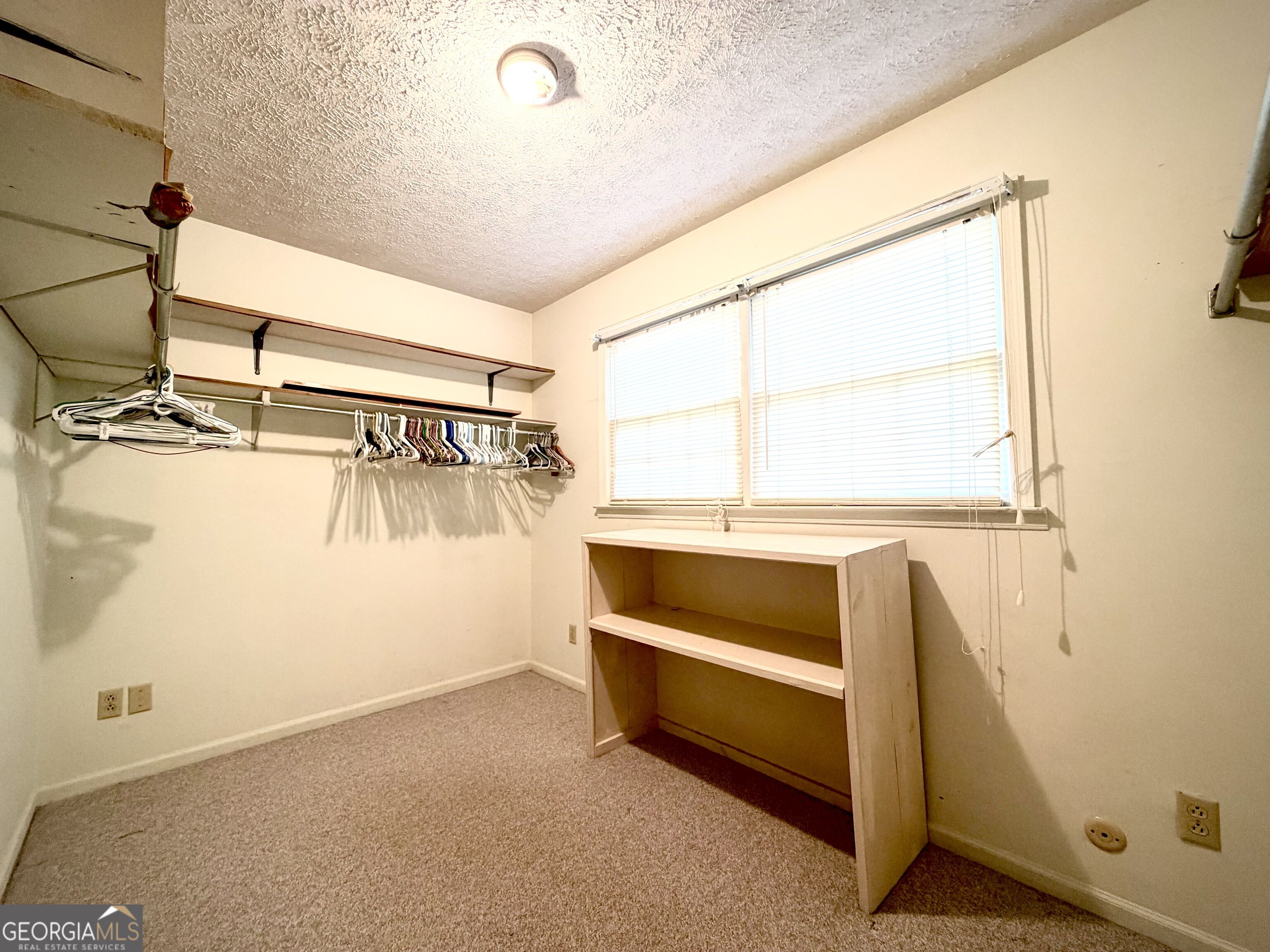 Walk-in closet with hanging rods, shelves, and a bright window with blinds.