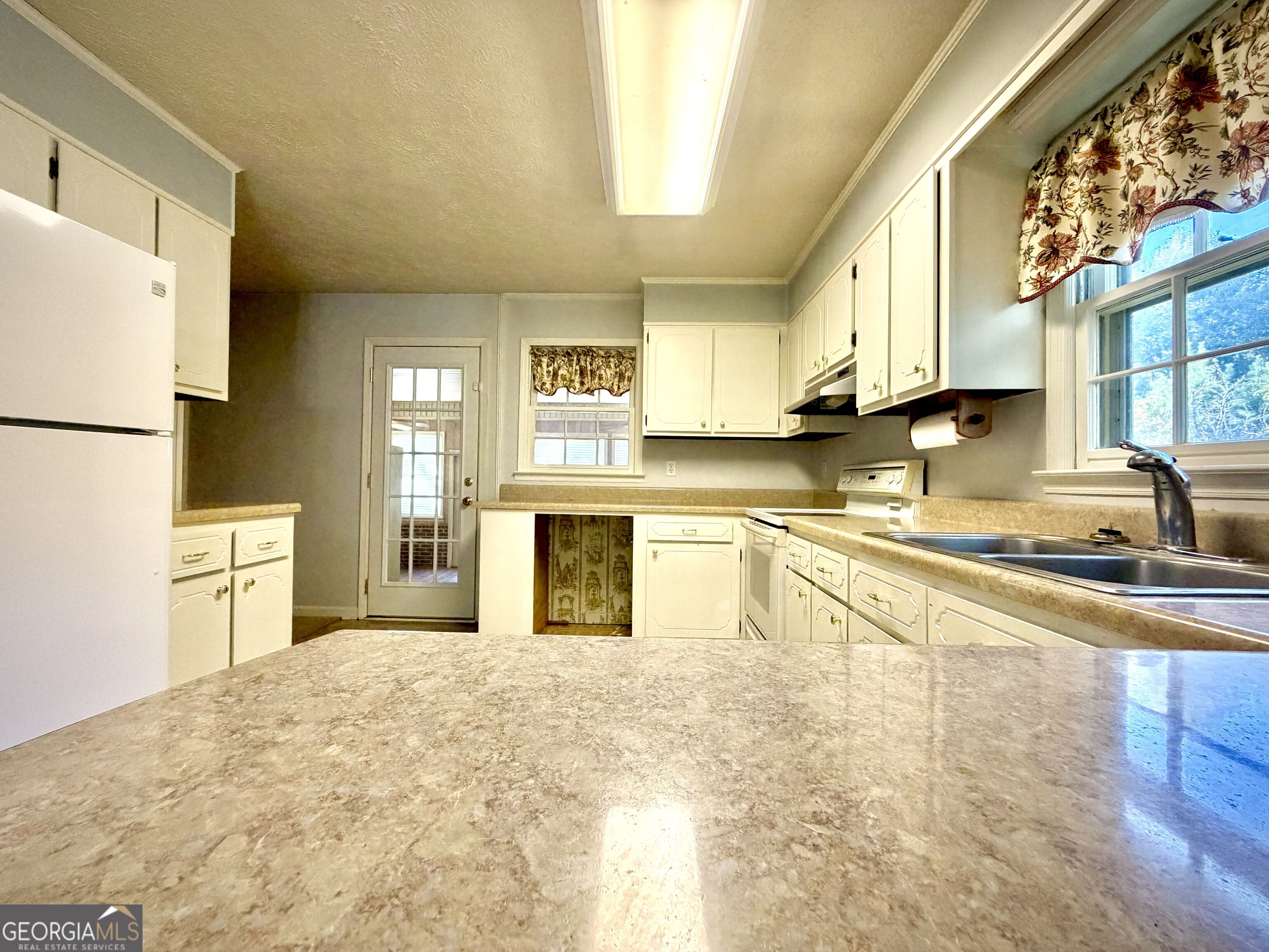 Kitchen with cream cabinets, tan countertops, a double sink, and floral curtains over the windows.