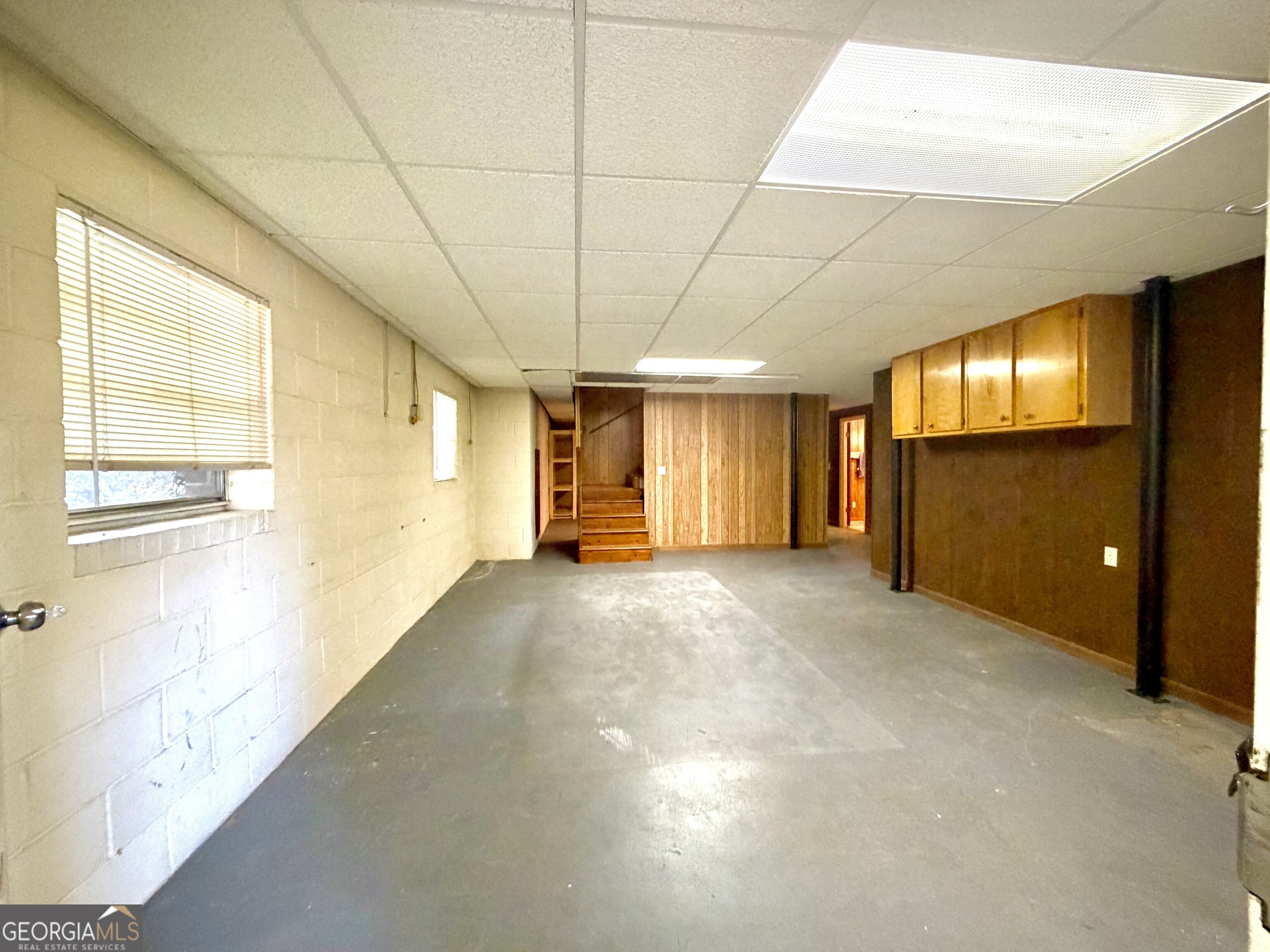 Basement room with concrete floor, wooden stairs, paneling, and built-in cabinets.