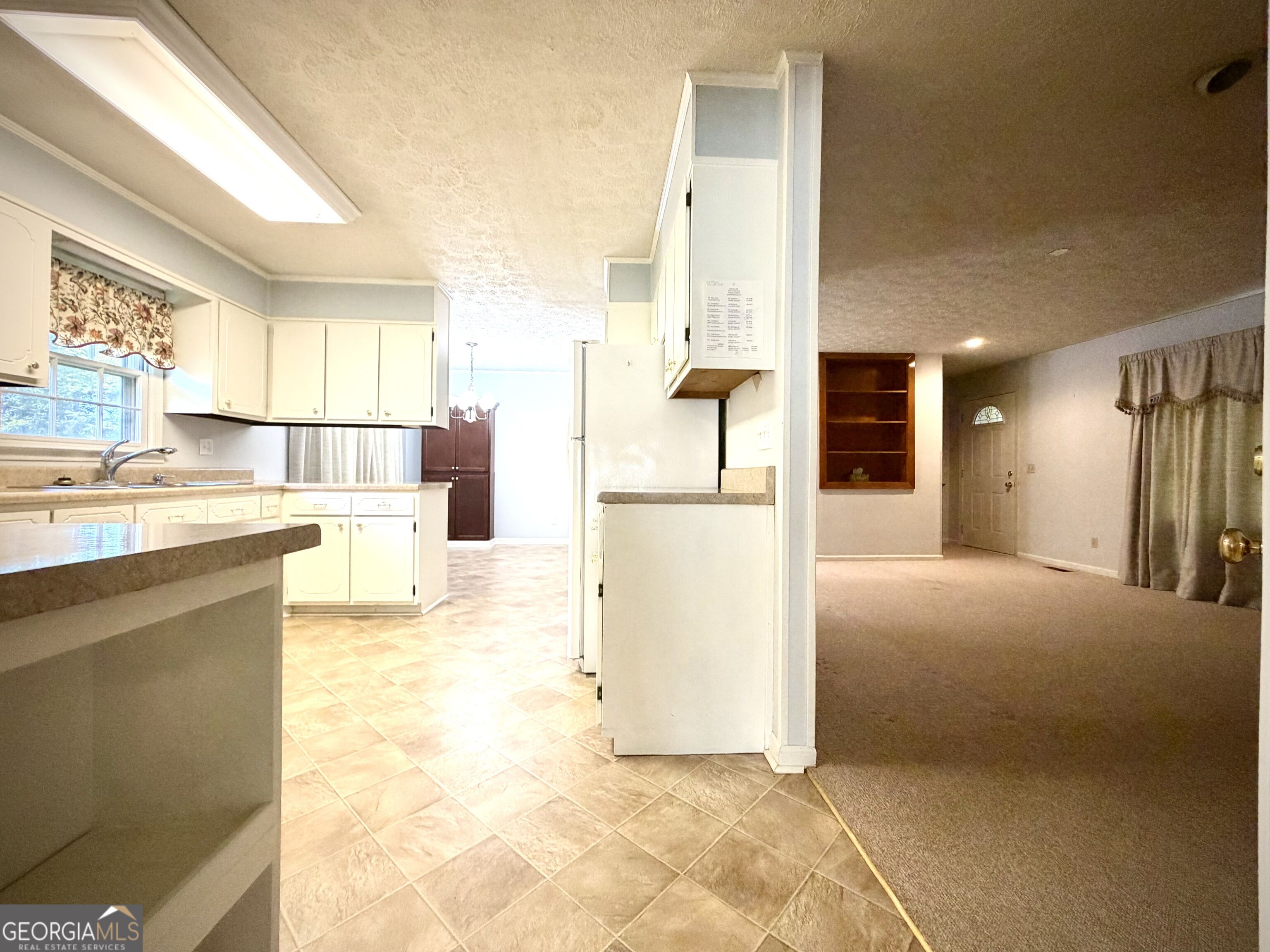Kitchen with white cabinets, tile floor, and breakfast bar opening into a carpeted living area.