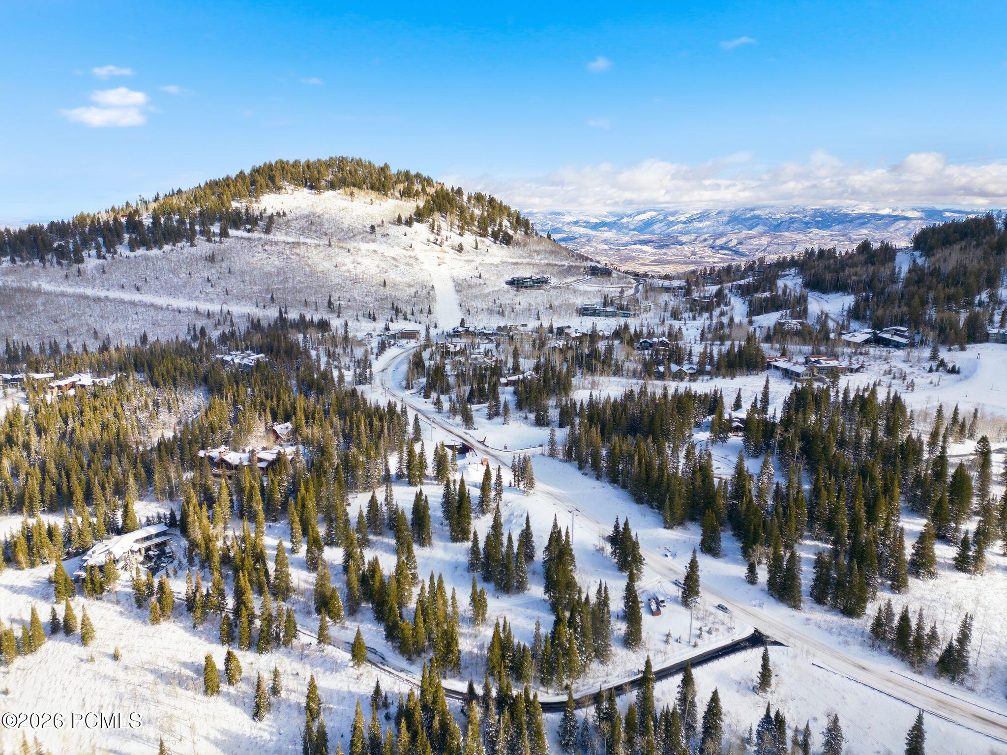Snow-covered mountain neighborhood with scattered homes, evergreen forest, winding roads, and distant ranges.