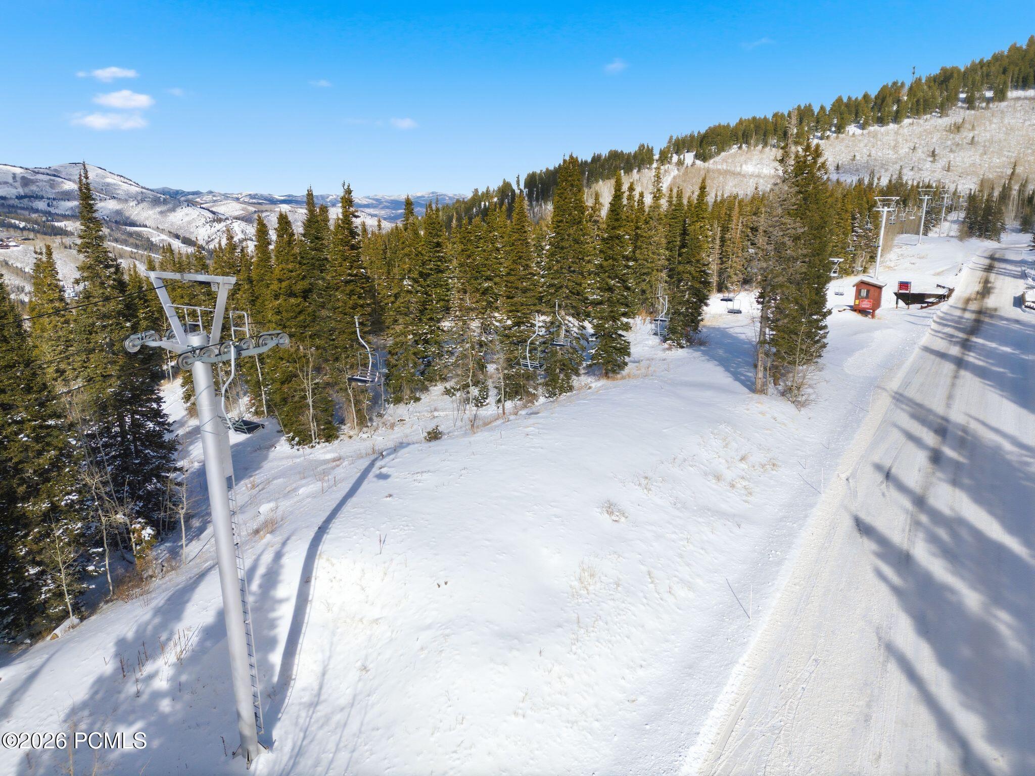 Snowy ski slope and chairlift among evergreens, with mountain ridges beyond.
