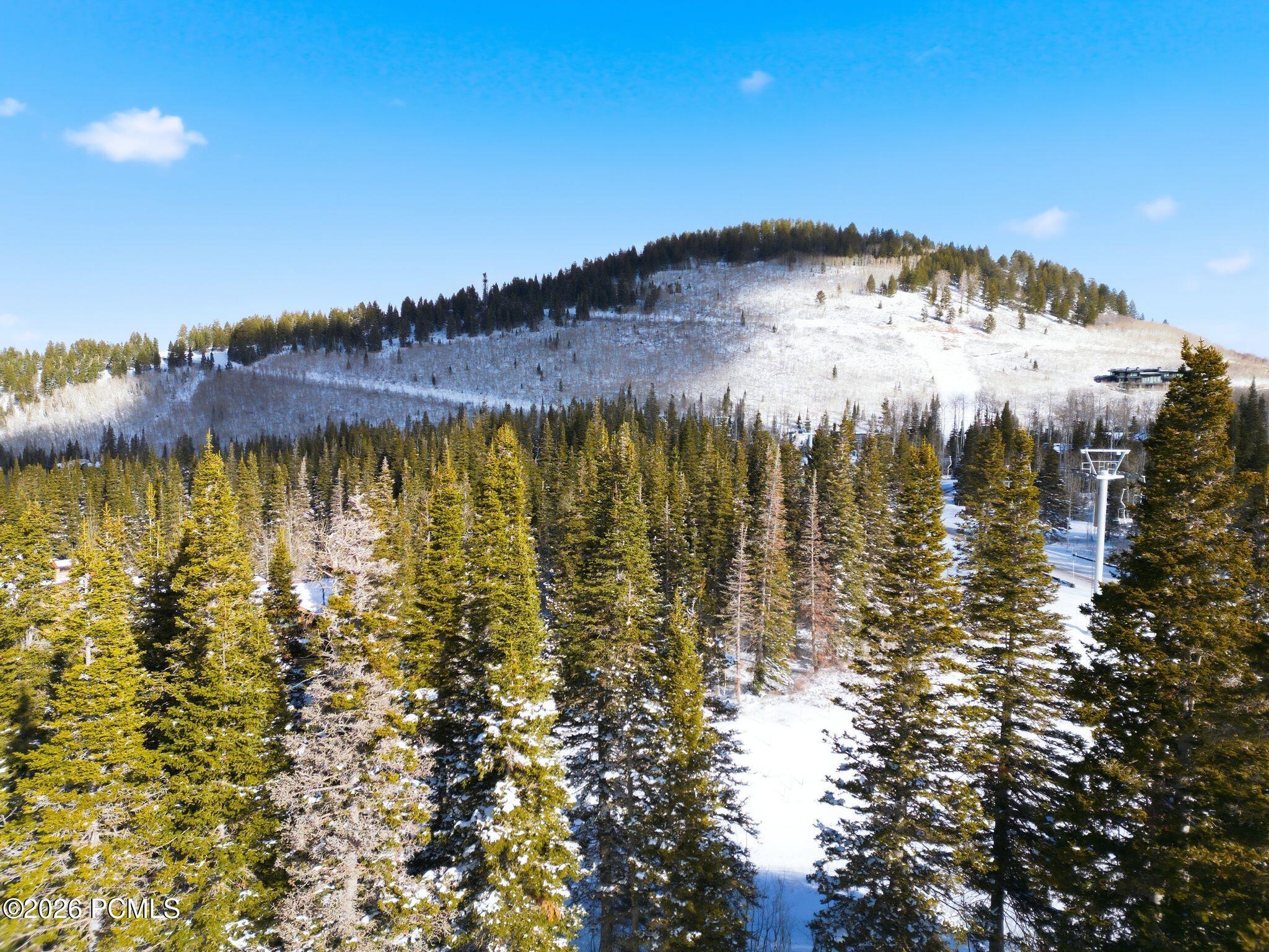 Snow-dusted mountain forest with a modern home on the hillside and a ski lift structure.