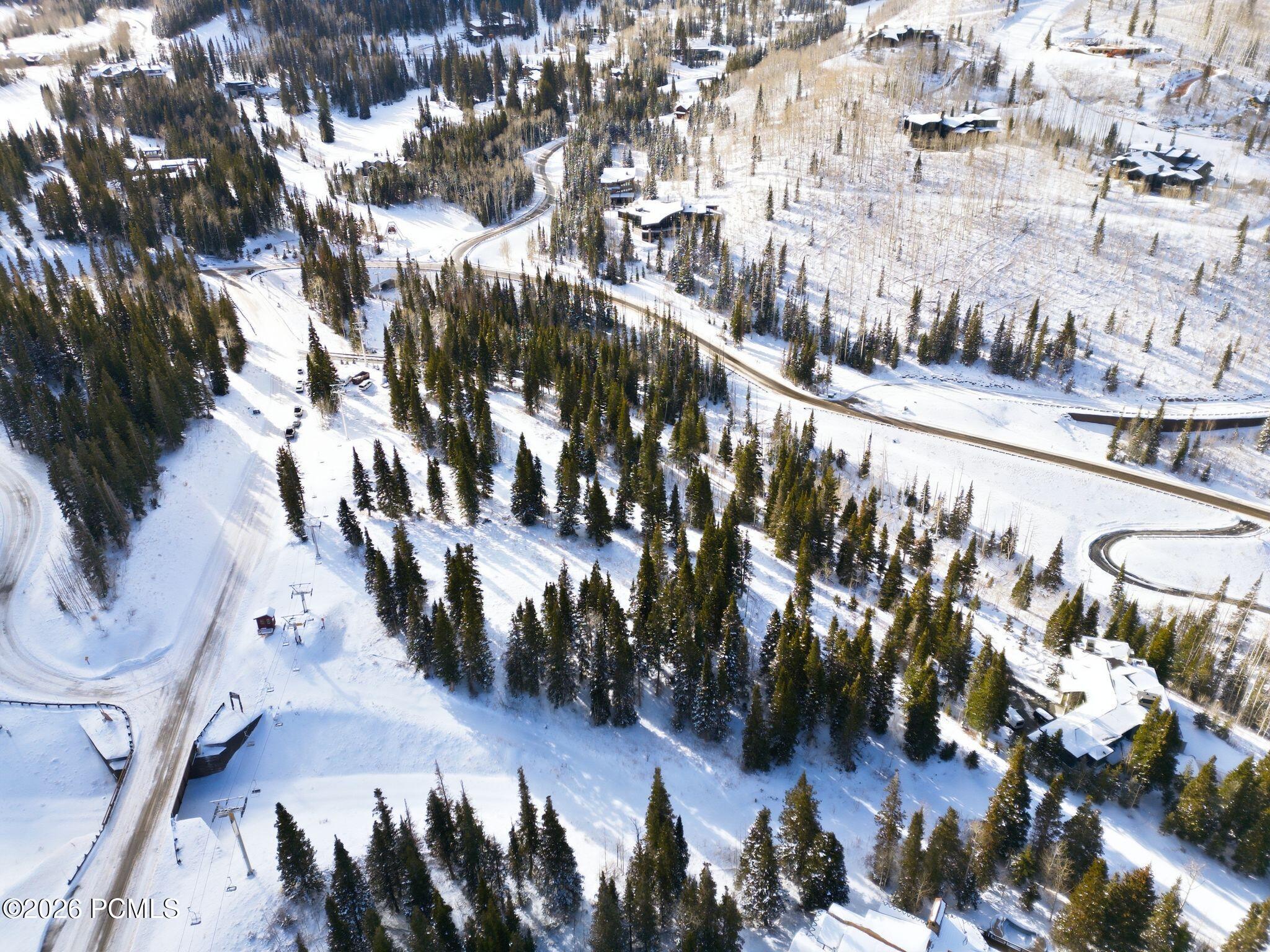 Aerial view of a snow-covered wooded property with nearby homes, curving roads, and ski-lift infrastructure.