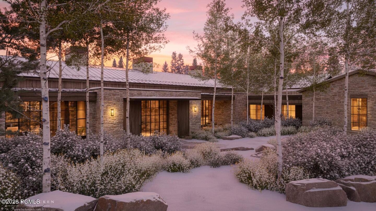 Stone house with a metal roof and glowing windows among snowy aspens at dusk.