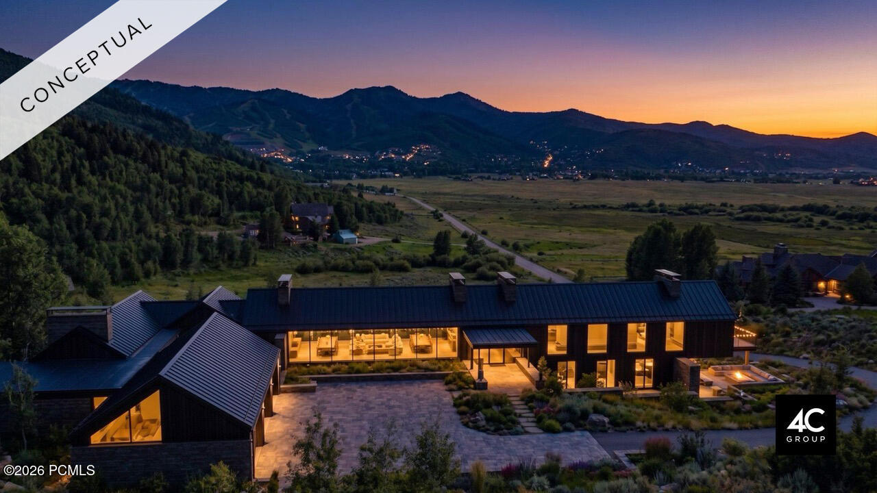 Modern home glowing at dusk beneath mountain ridges, with valley views and a broad stone patio.