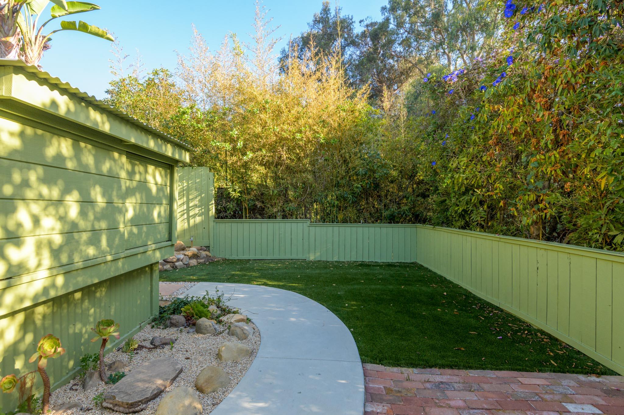 Enclosed backyard with artificial turf, a curved walkway, and a gravel succulent garden.