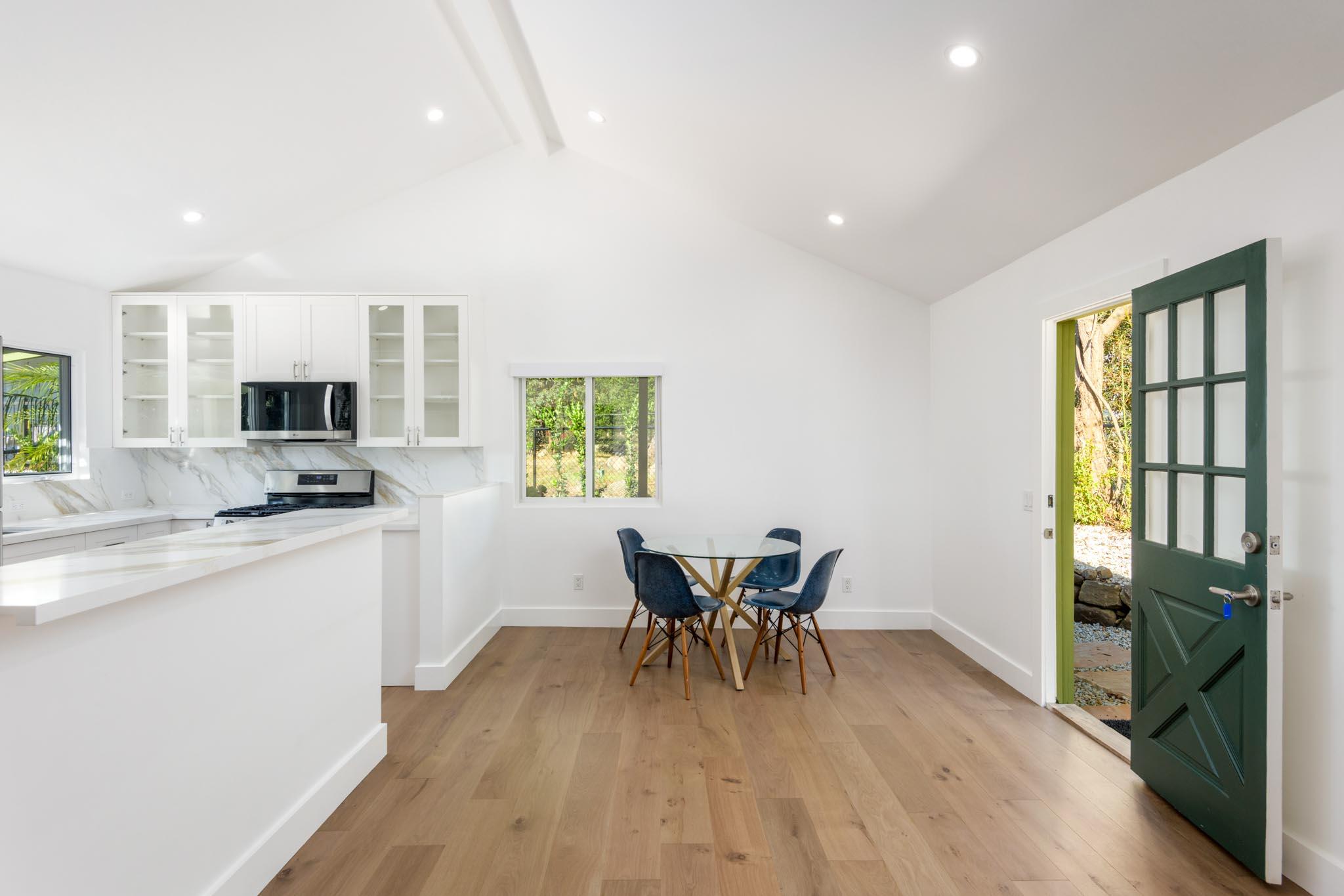 Bright kitchen and dining area with a round table, blue chairs, and an open dark green door.