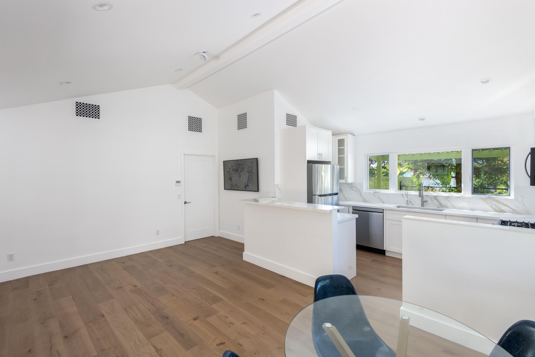 Open kitchen with white cabinetry, stainless appliances, large garden-facing windows, and wood flooring.