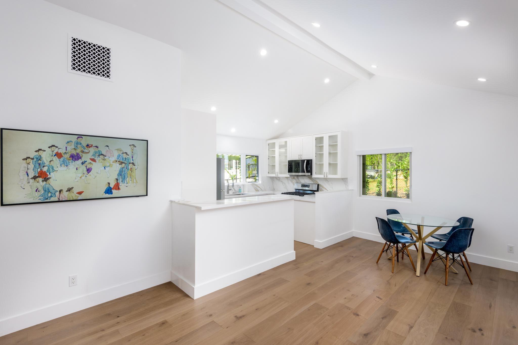 Open-plan kitchen and dining area with white cabinetry, a peninsula, and a glass table with blue chairs.