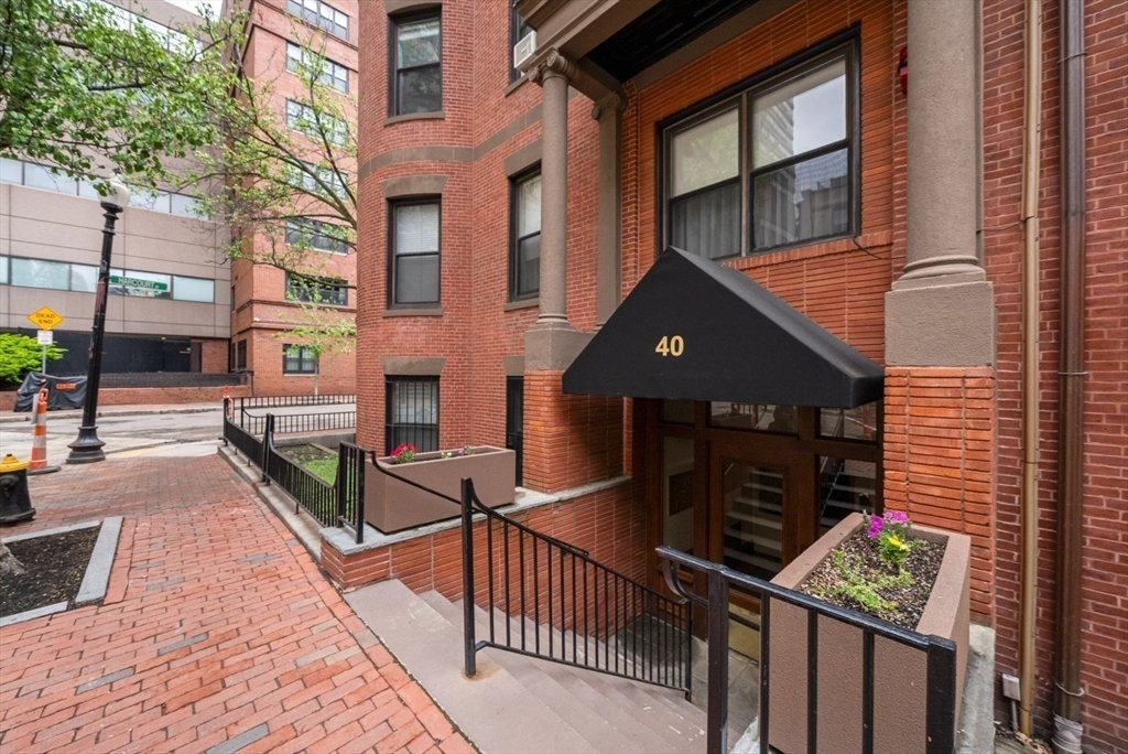 Red-brick building entrance with a black awning marked 40 and flower planters.