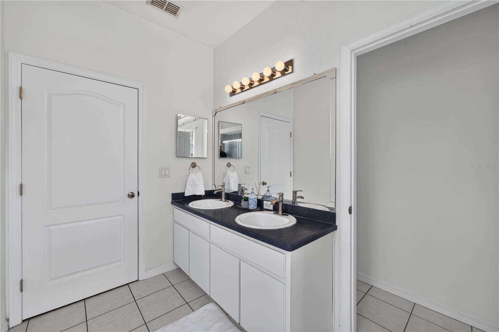 Bathroom with a white double vanity, dark countertop, large mirror, and warm vanity lights.