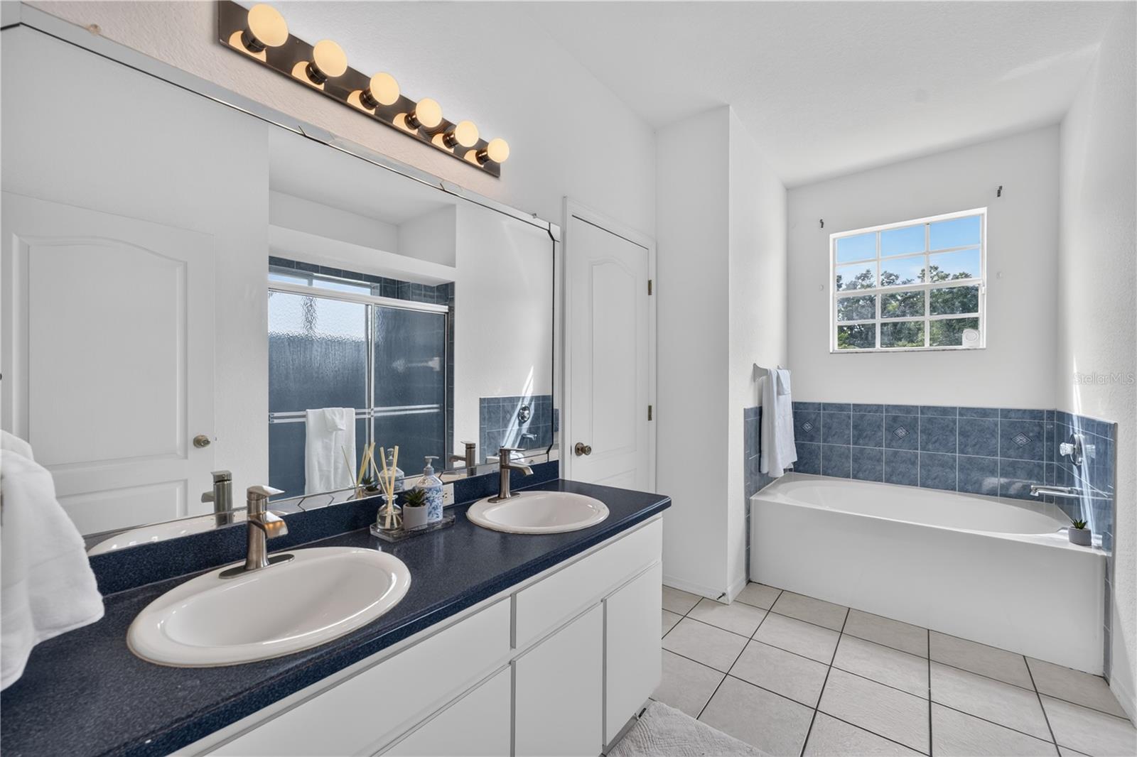 Bathroom with a double-sink vanity and a bathtub beneath a large window.