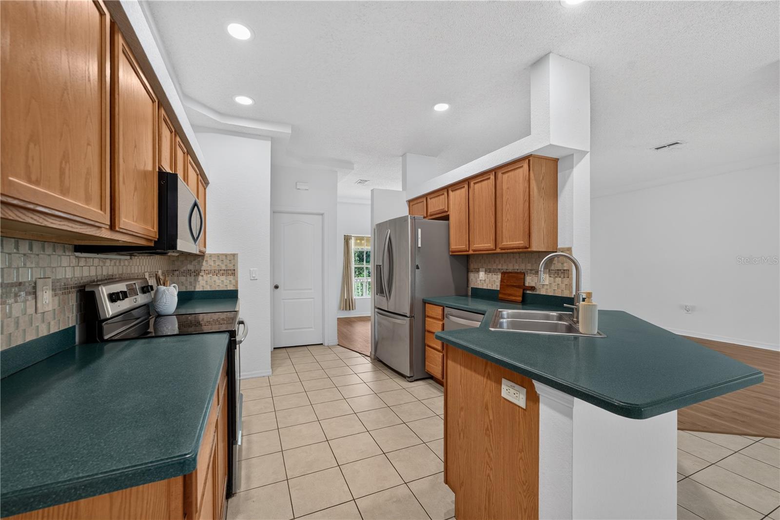 Kitchen with oak cabinets, teal countertops, and a stainless steel refrigerator.