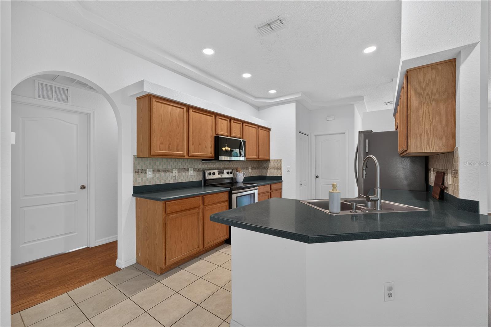 Kitchen with wood cabinets, dark countertops, stainless steel appliances, and a large island sink.