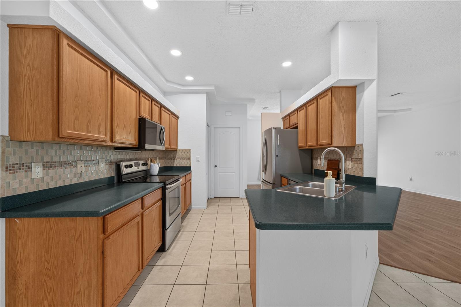 Kitchen with wood cabinets, dark green counters, stainless steel appliances, and a large island sink.