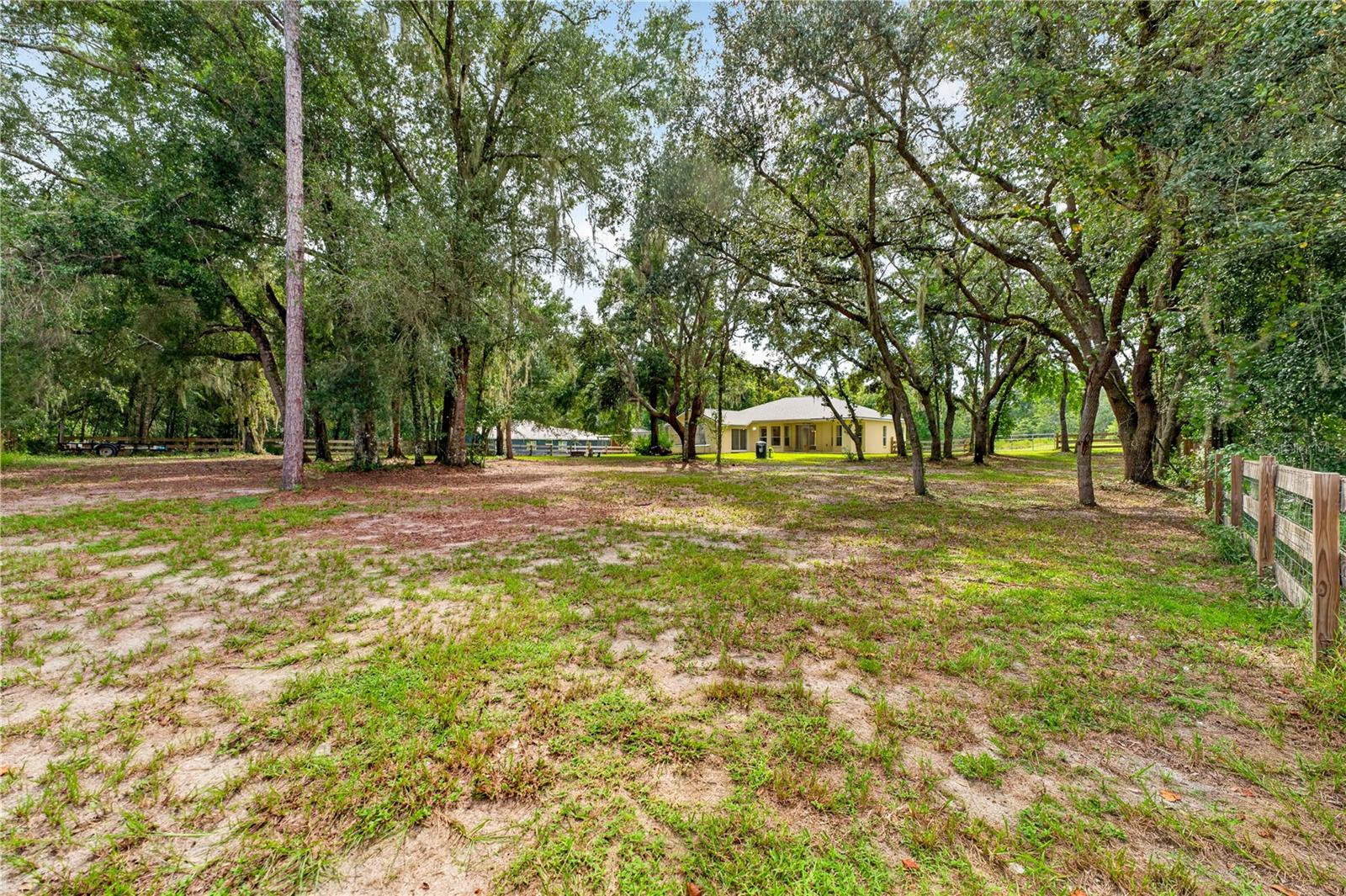 Single-story home set back among mature trees on a spacious sandy lot.