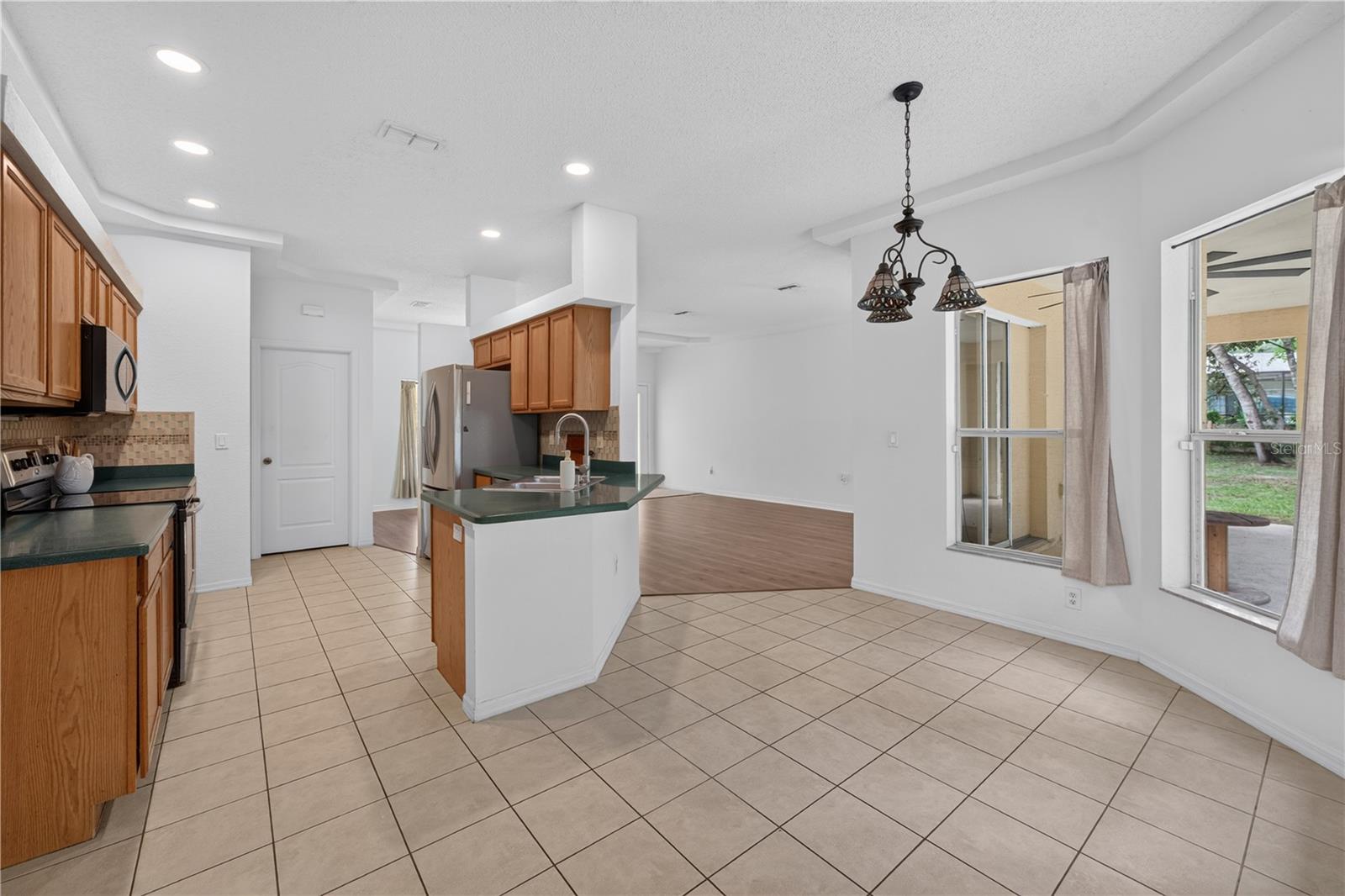 Kitchen and dining area with oak cabinets, a central peninsula, and beige tile floors.