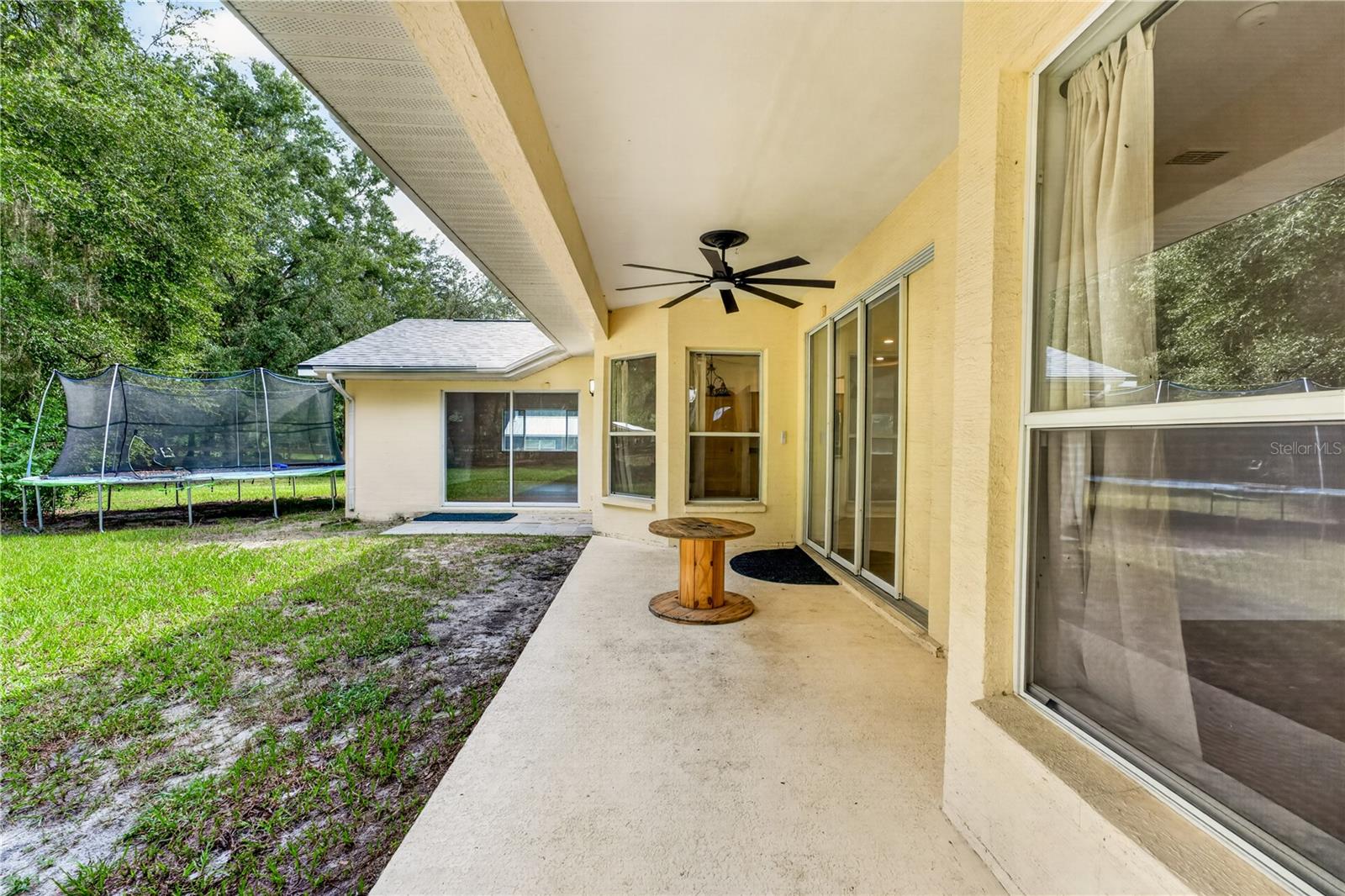 Covered patio with ceiling fan and sliding doors overlooking a grassy yard and trampoline.