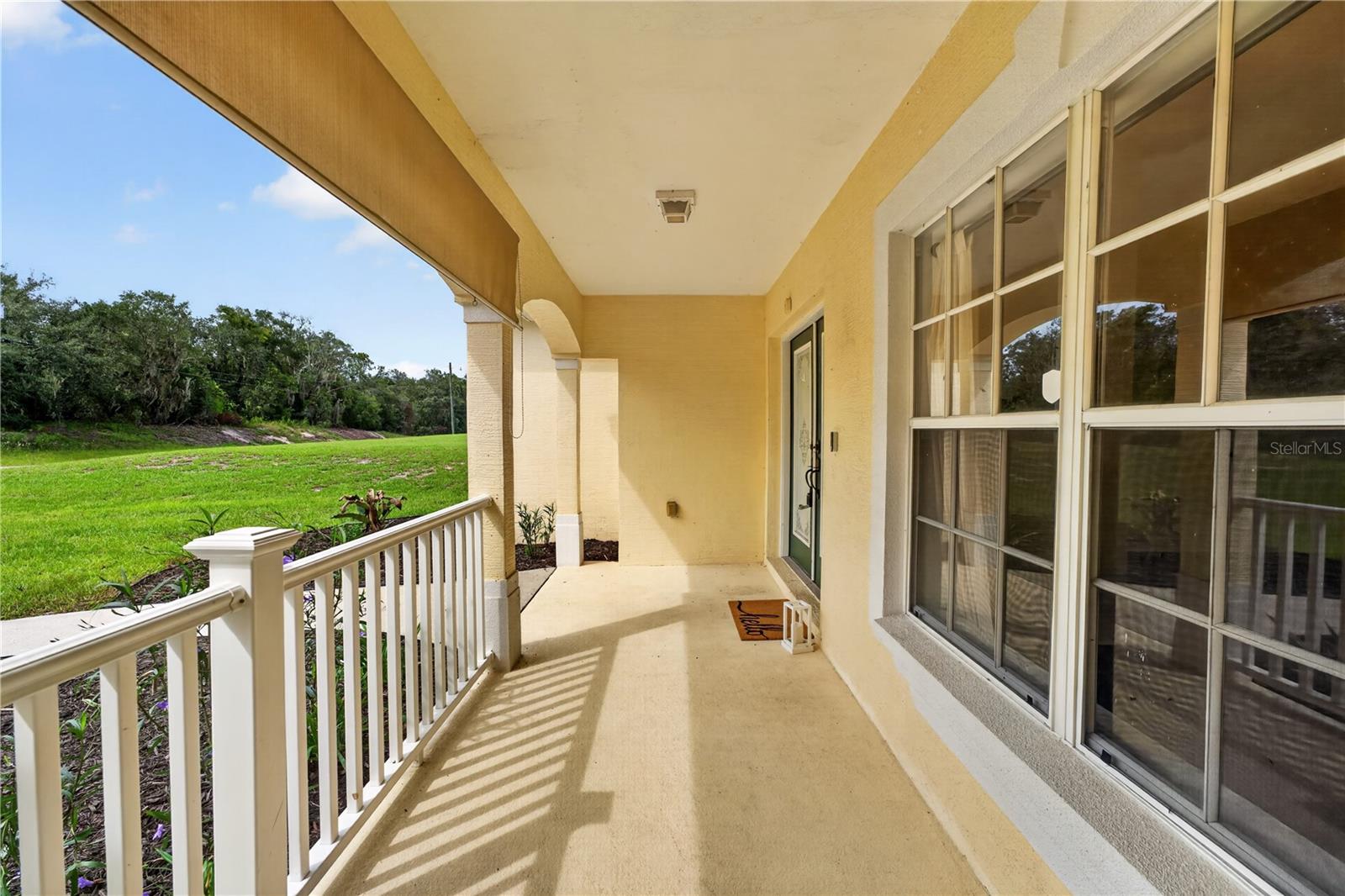 Covered front porch with white railing, large windows, and a view of the lawn.